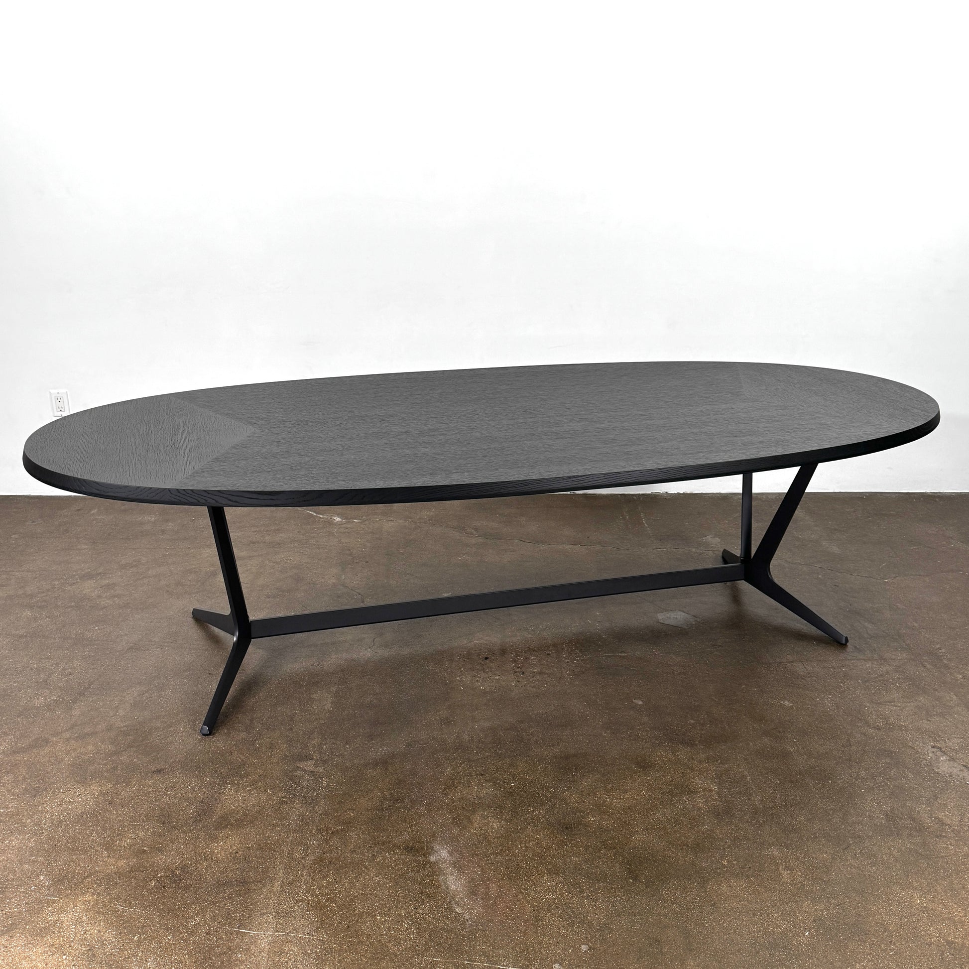 A spacious Maxalto Astrum Dining Table by Maxalto with black oak finish and bronze nickel base is paired with eight evenly arranged dark brown chairs in a minimalist setting.