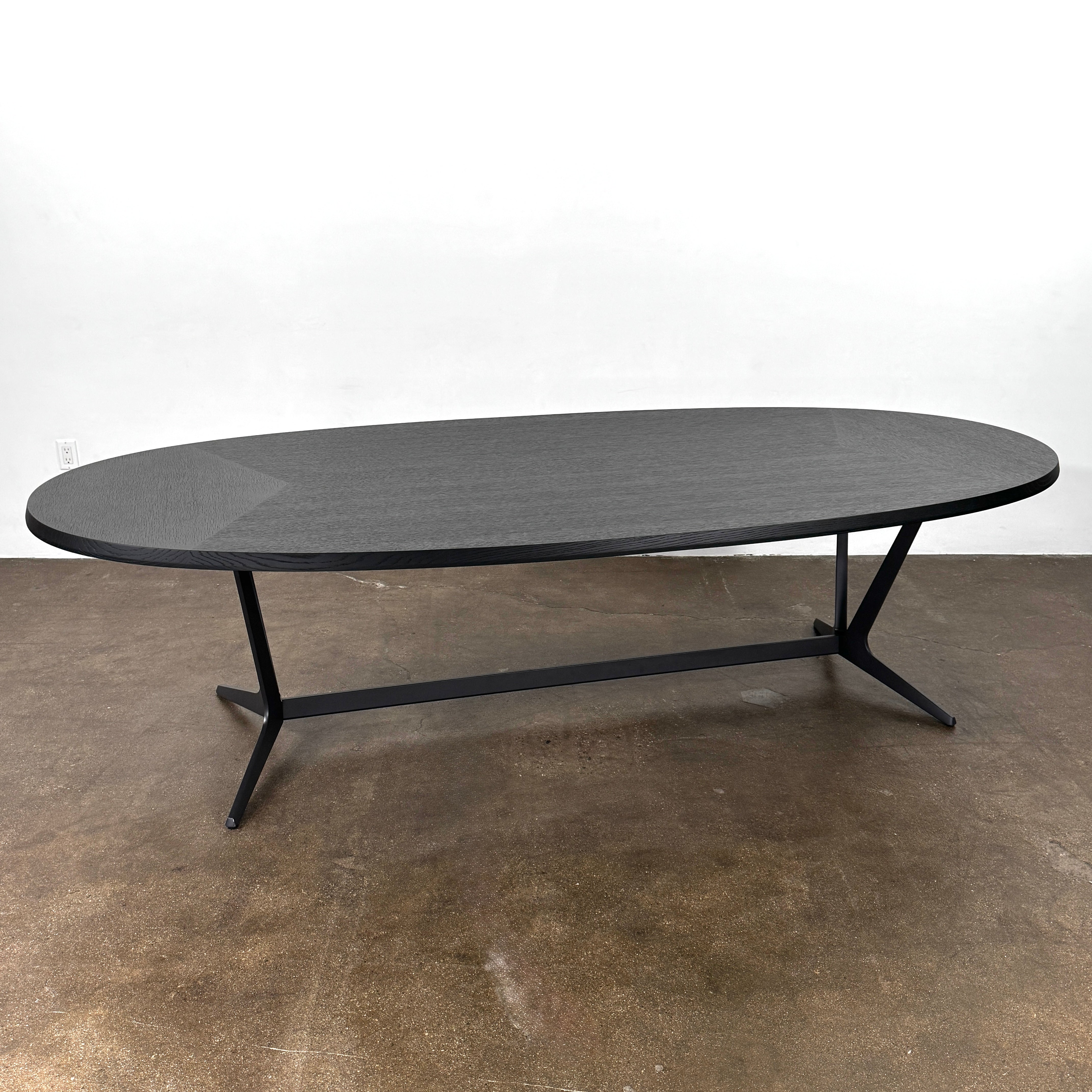 A spacious Maxalto Astrum Dining Table by Maxalto with black oak finish and bronze nickel base is paired with eight evenly arranged dark brown chairs in a minimalist setting.