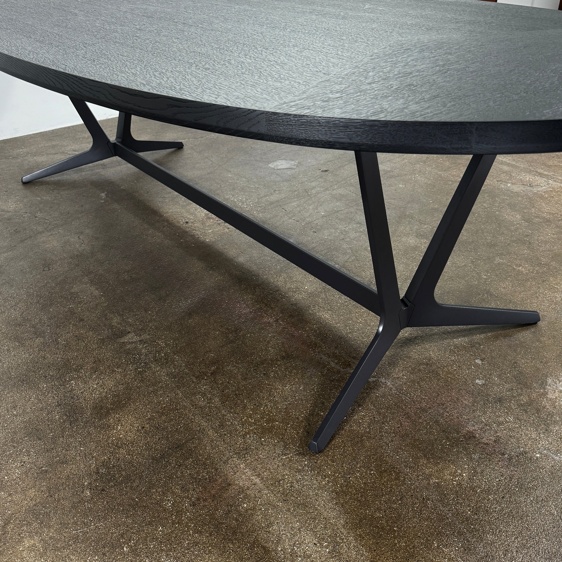 A spacious Maxalto Astrum Dining Table by Maxalto with black oak finish and bronze nickel base is paired with eight evenly arranged dark brown chairs in a minimalist setting.