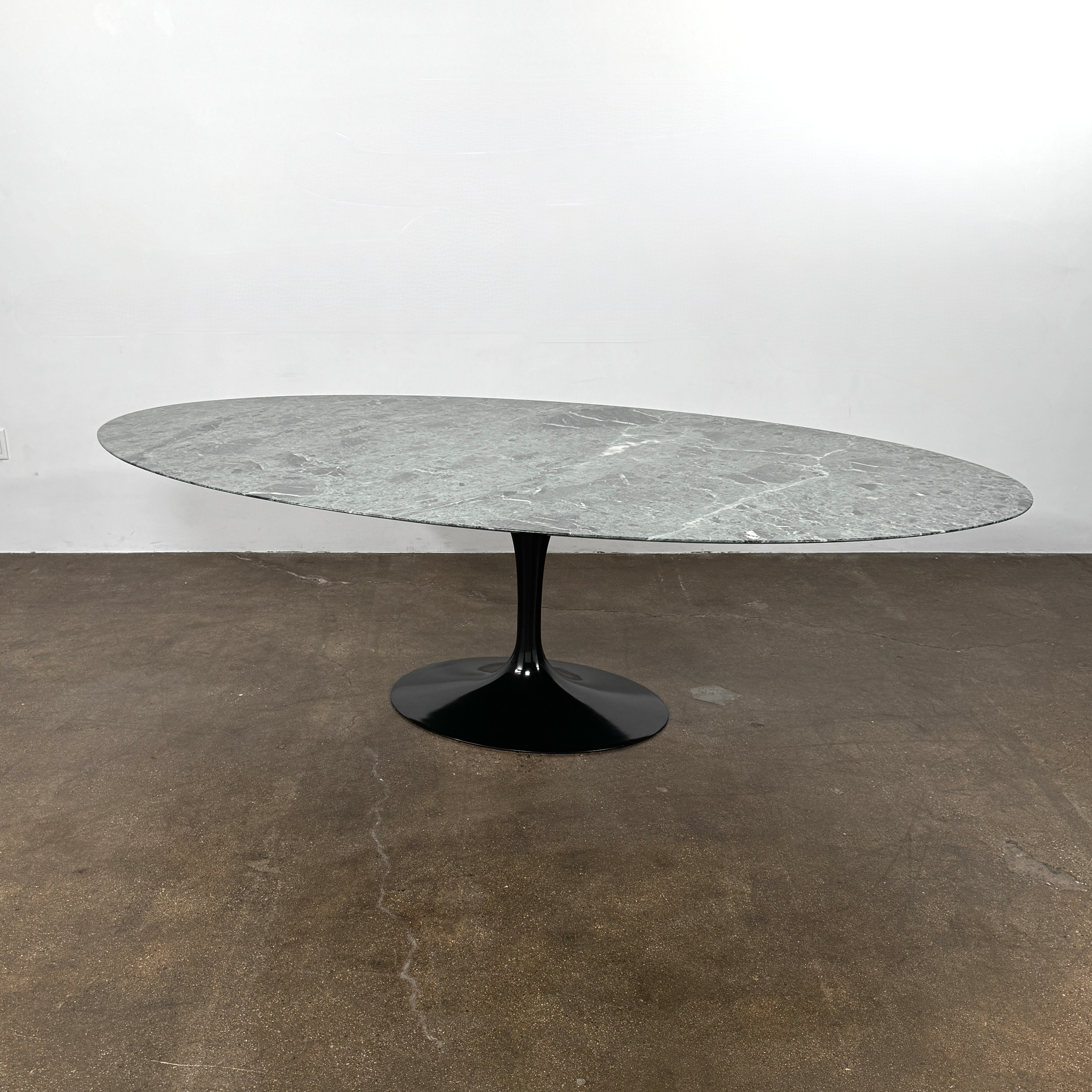 The Knoll Oval Verde Alpi Marble Saarinen Table features a gray marble top and a black pedestal base, inspired by the classic design, set against a plain white background.