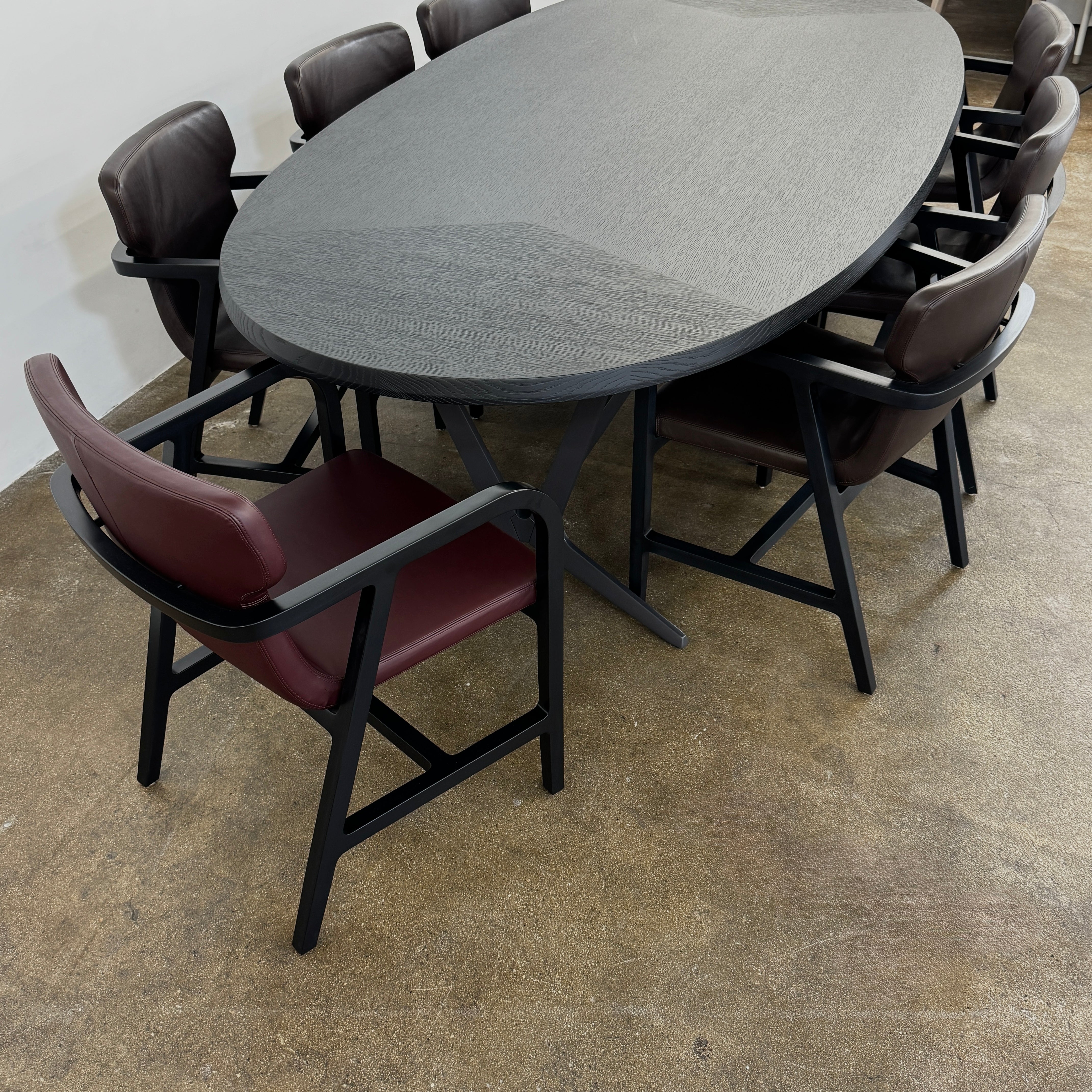 A spacious Maxalto Astrum Dining Table by Maxalto with black oak finish and bronze nickel base is paired with eight evenly arranged dark brown chairs in a minimalist setting.