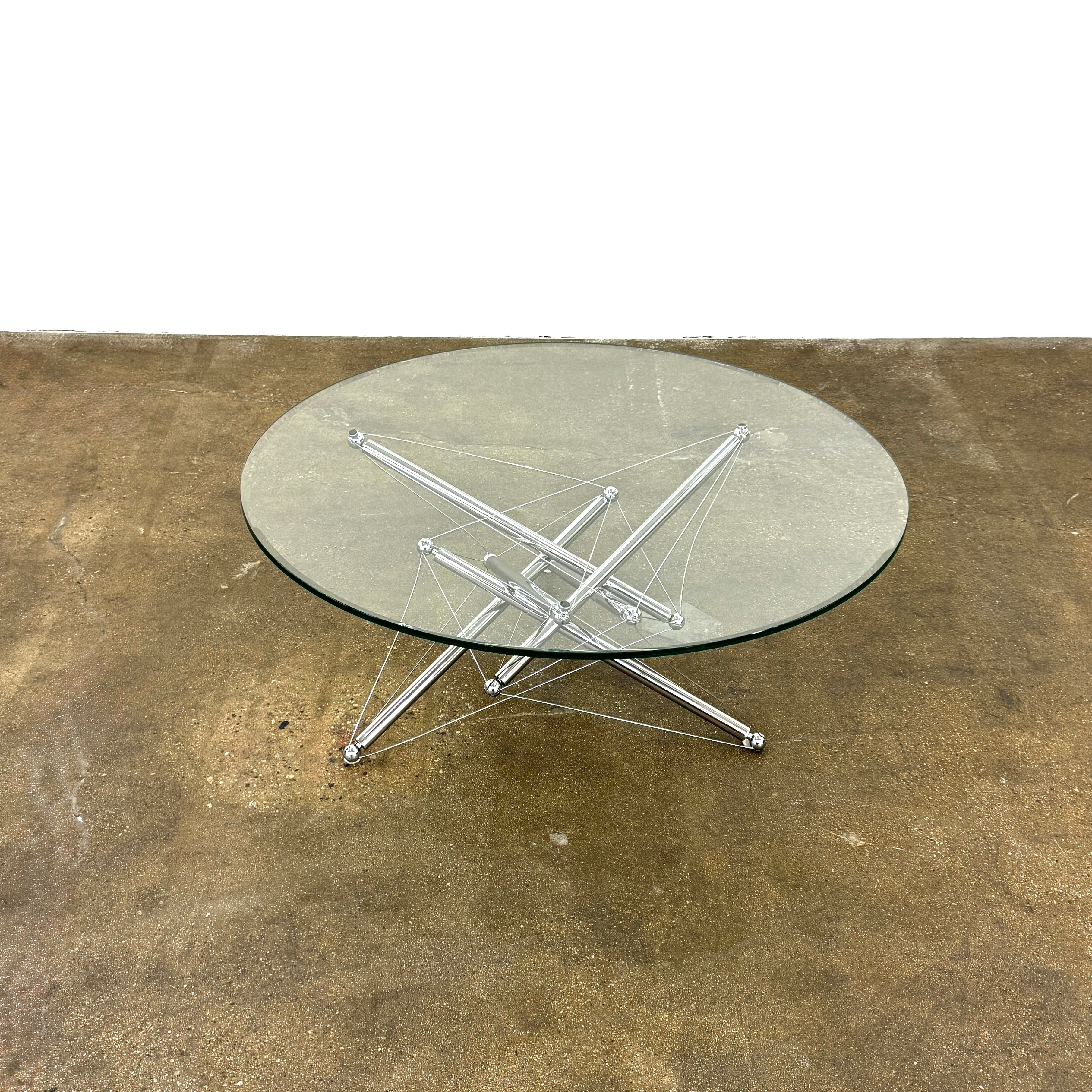 The Cassina "Tensegrity" 713 Cocktail Table features a round glass top and a geometric chrome metal base with tension cables, displayed on a plain white background.