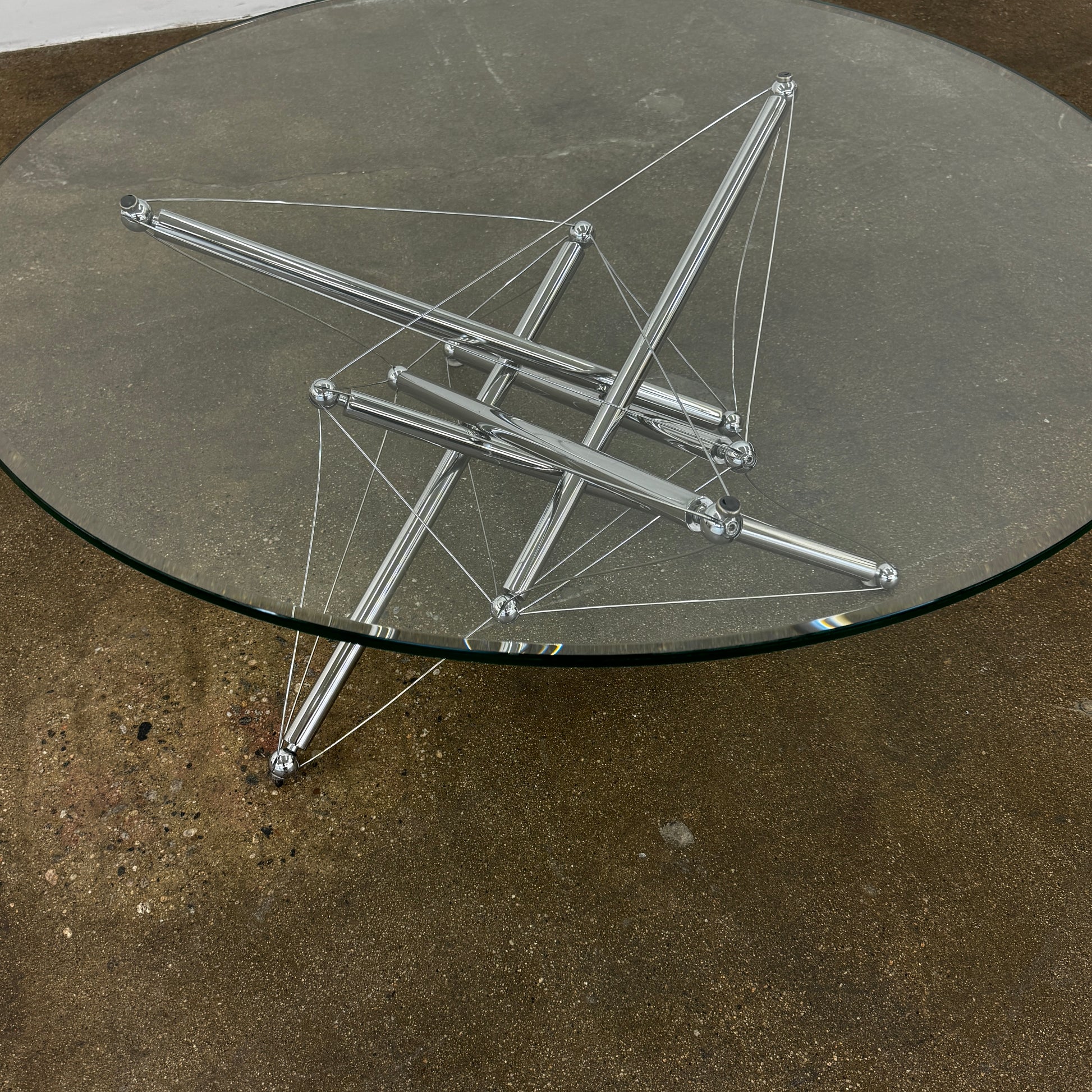 The Cassina "Tensegrity" 713 Cocktail Table features a round glass top and a geometric chrome metal base with tension cables, displayed on a plain white background.