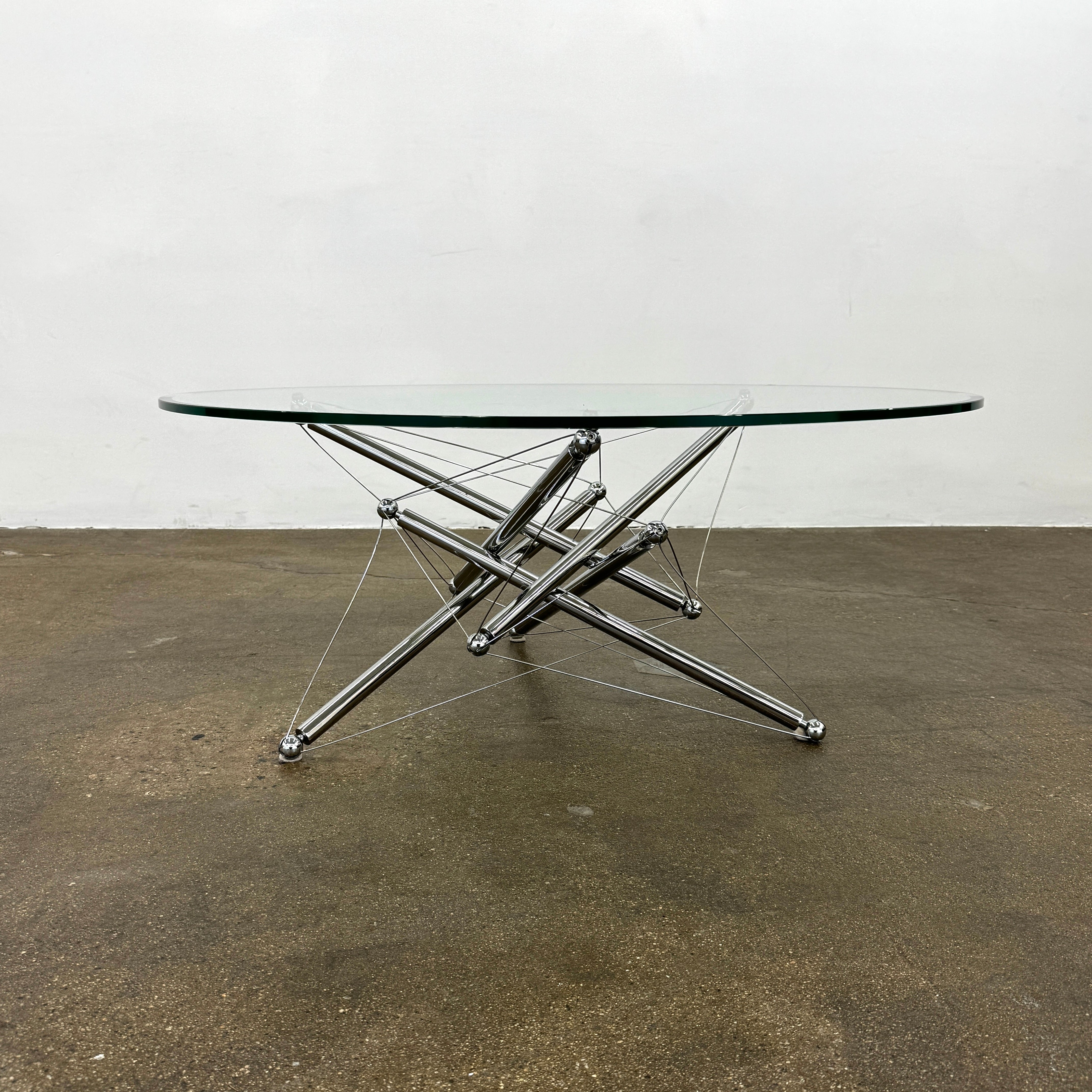 The Cassina "Tensegrity" 713 Cocktail Table features a round glass top and a geometric chrome metal base with tension cables, displayed on a plain white background.