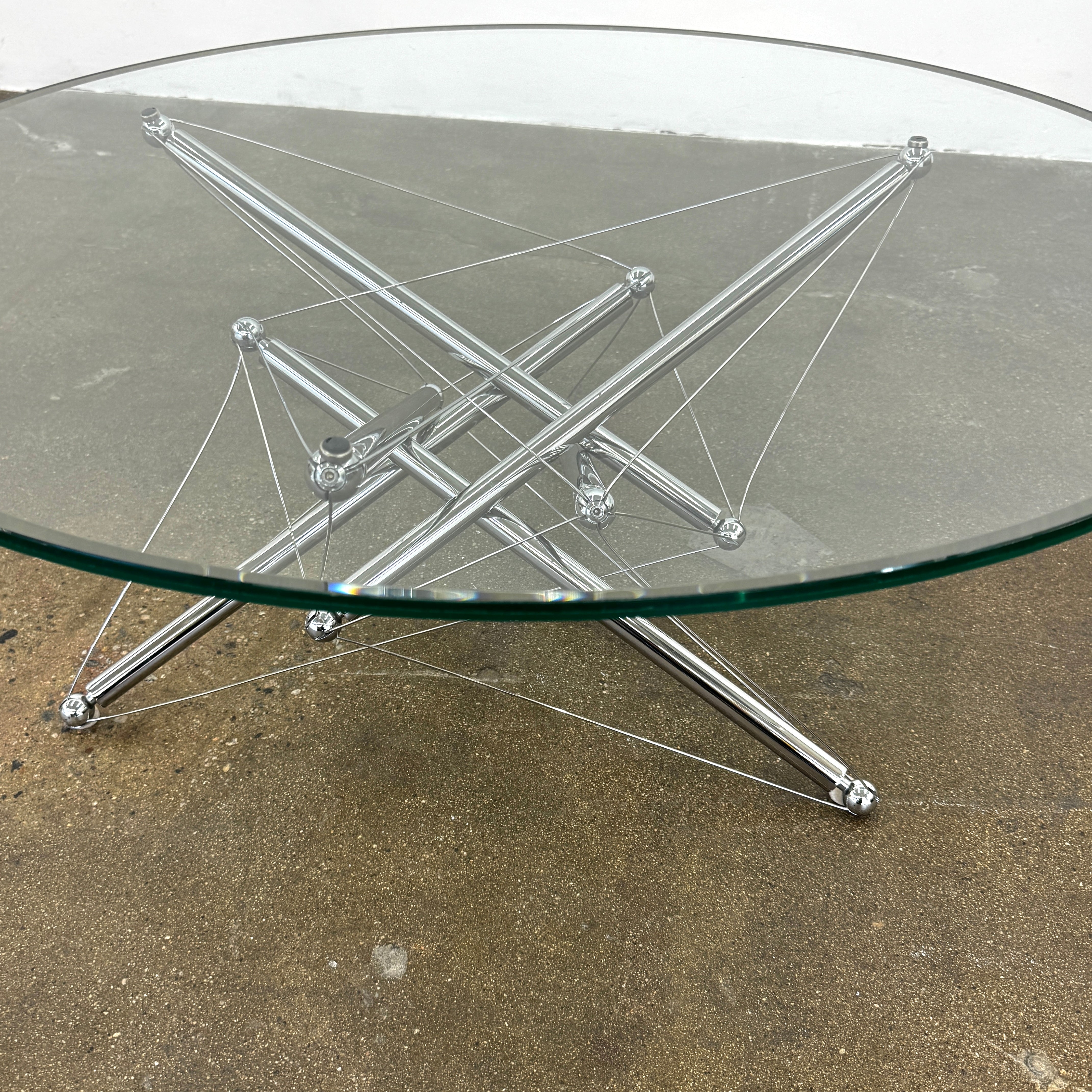 The Cassina "Tensegrity" 713 Cocktail Table features a round glass top and a geometric chrome metal base with tension cables, displayed on a plain white background.