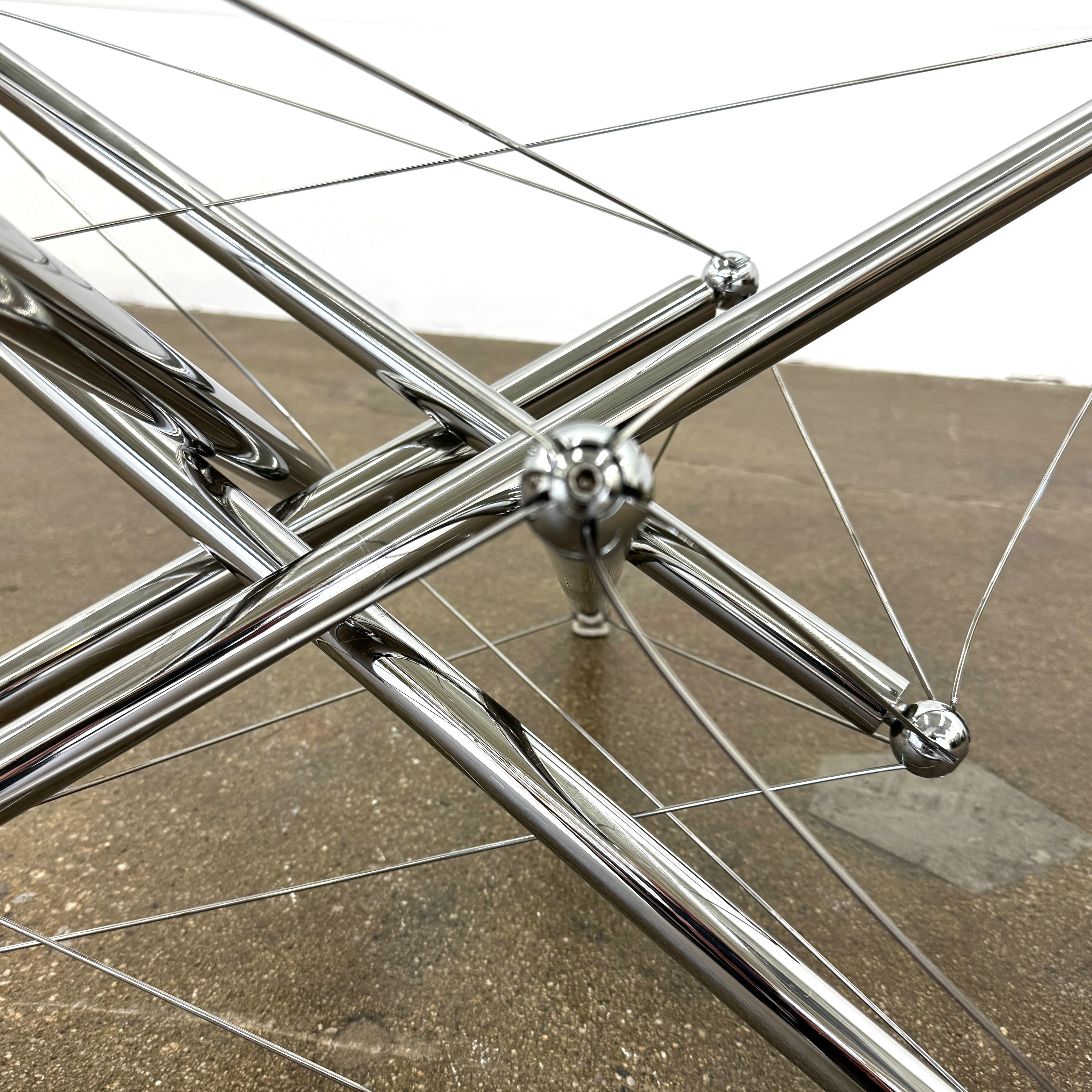 The Cassina "Tensegrity" 713 Cocktail Table features a round glass top and a geometric chrome metal base with tension cables, displayed on a plain white background.