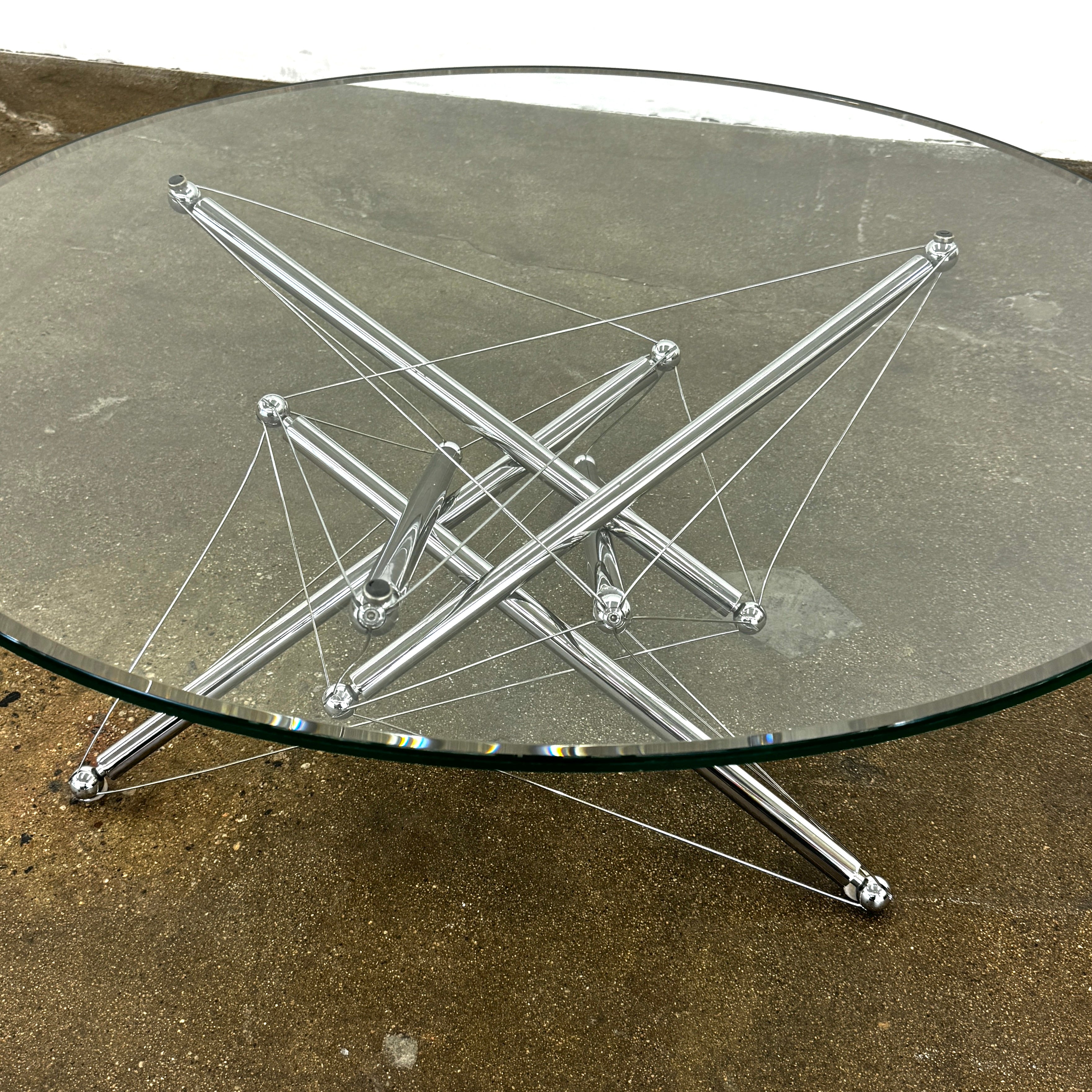 The Cassina "Tensegrity" 713 Cocktail Table features a round glass top and a geometric chrome metal base with tension cables, displayed on a plain white background.