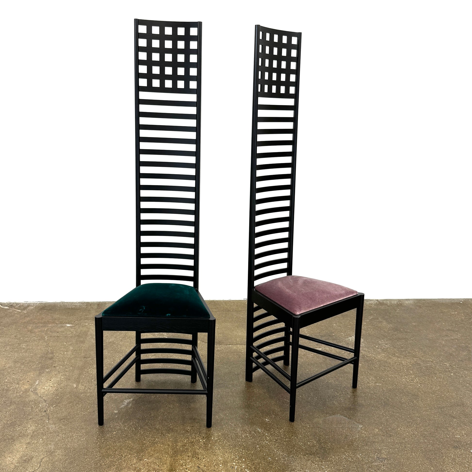 A pair of Cassina 292 Hill House Chairs by Charles R. Mackintosh, with black slatted frames—one featuring a burgundy seat cushion, the other dark green—showcasing Cassina's modernist design against a plain white background.