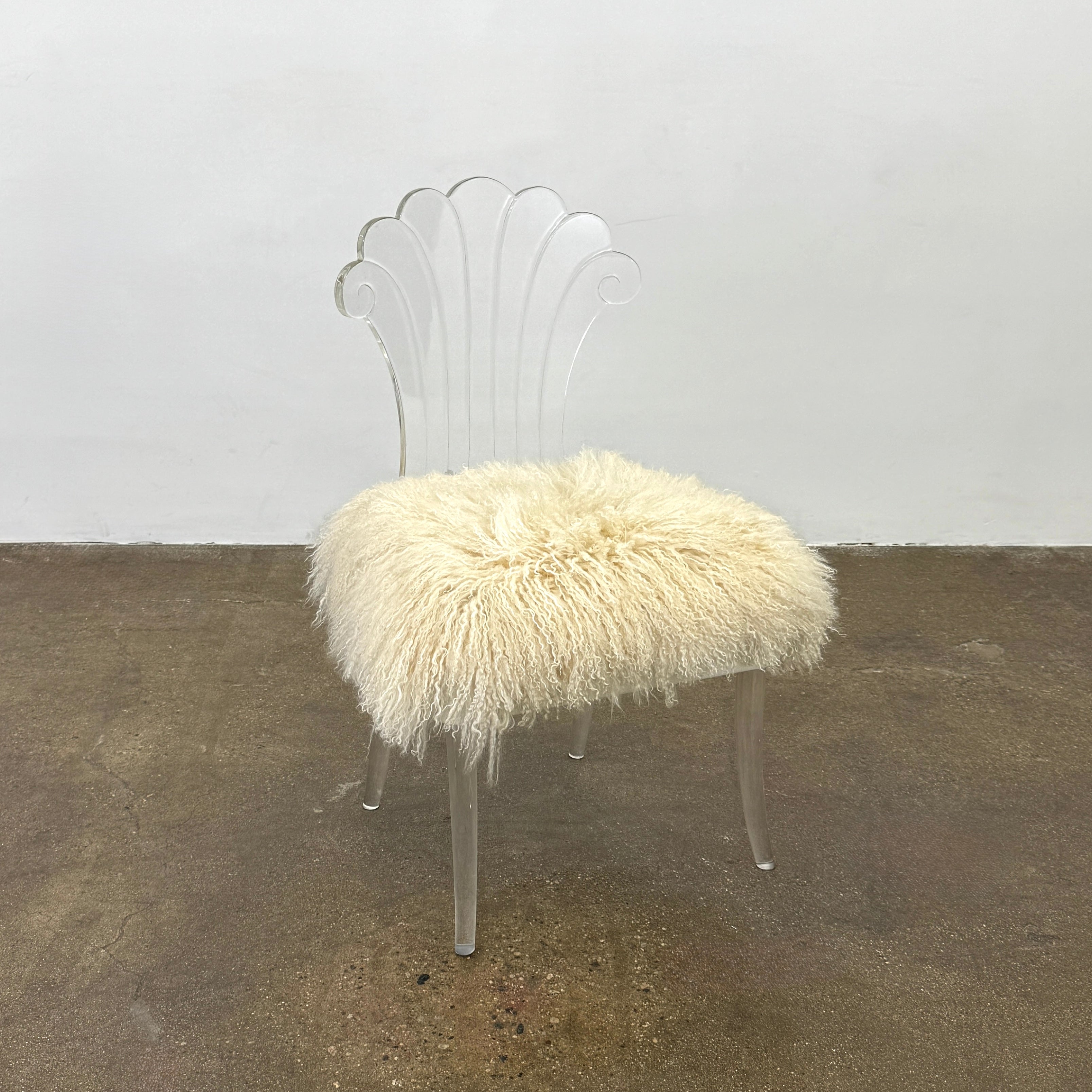 Two white Vintage Elsie de Wolfe Lucite Chairs with elegant fan-shaped backs and plush beige sheepskin seats are displayed against a plain white background.