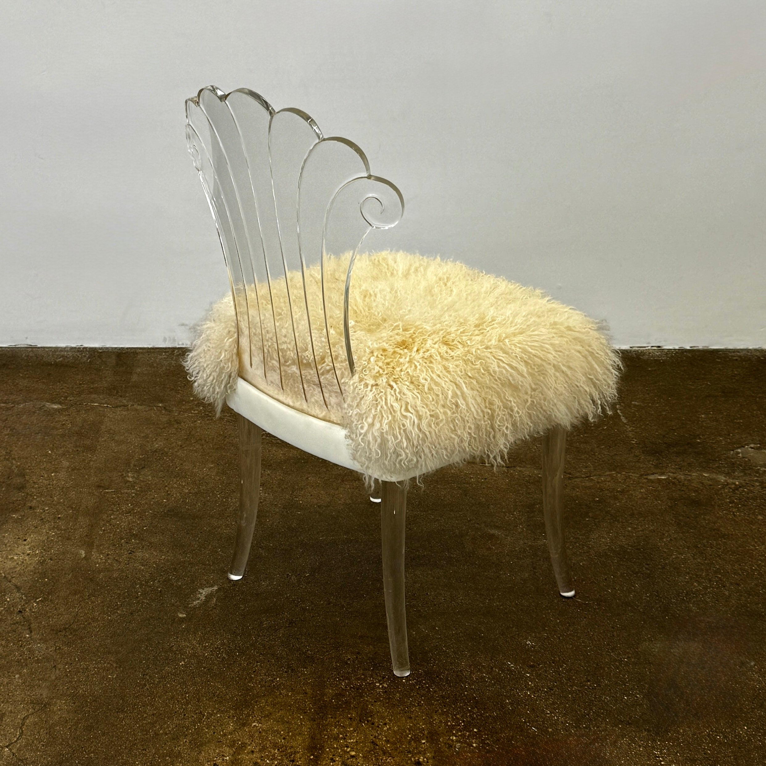 Two white Vintage Elsie de Wolfe Lucite Chairs with elegant fan-shaped backs and plush beige sheepskin seats are displayed against a plain white background.