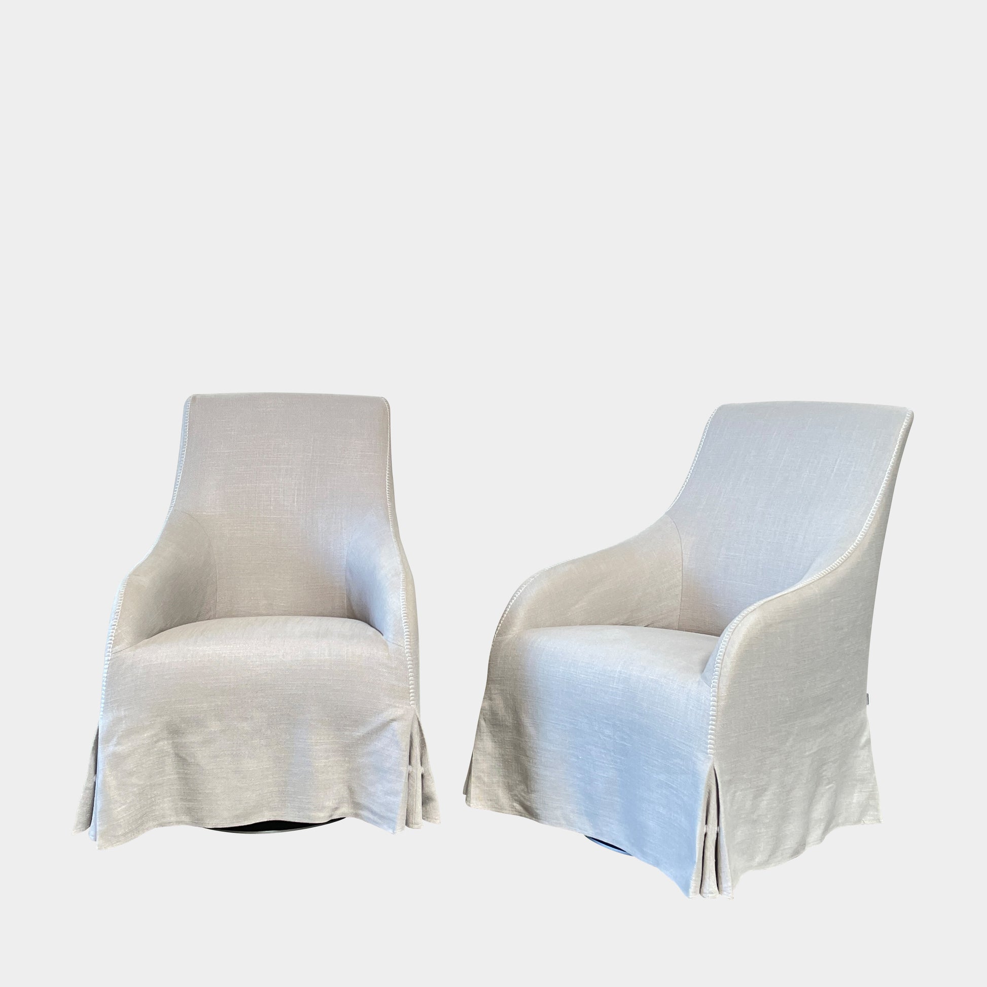 The beige upholstered chair, similar to the Maxalto Agathos Swivel Lounge Chairs, showcases a high back and a skirted bottom against a plain background.