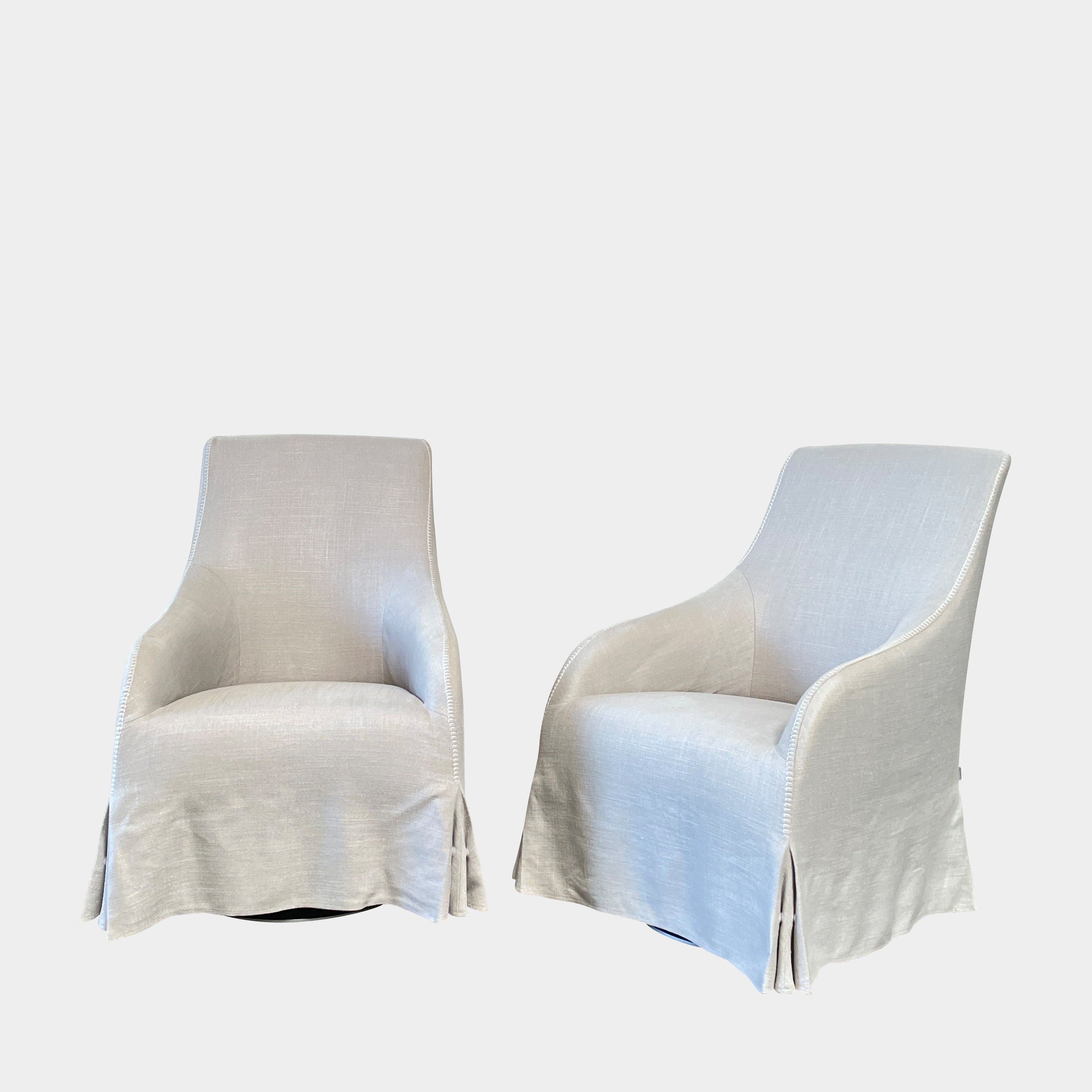 The beige upholstered chair, similar to the Maxalto Agathos Swivel Lounge Chairs, showcases a high back and a skirted bottom against a plain background.