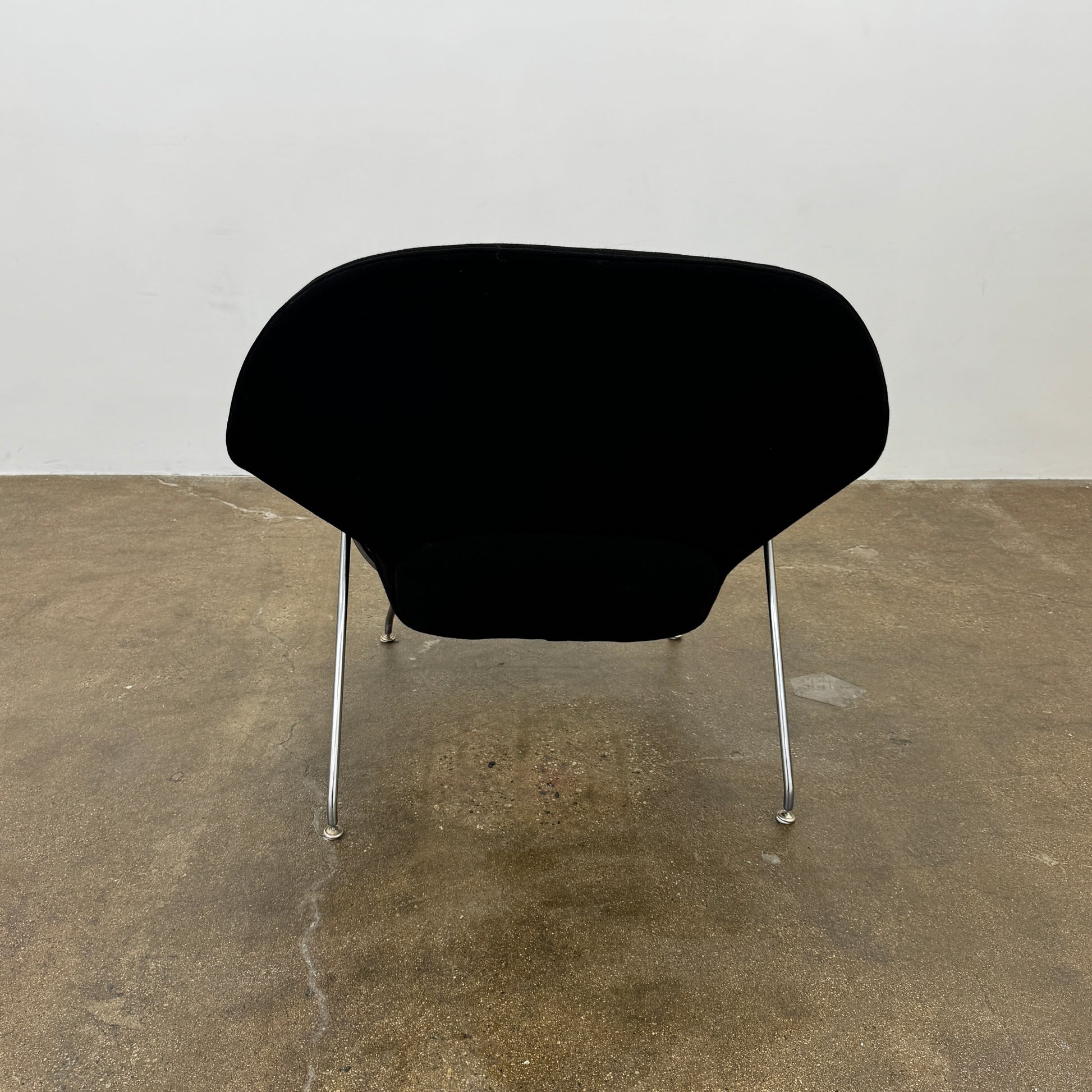The Knoll Womb Chair by Knoll features a black curved seat, padded cushion, and metal legs, drawing inspiration from midcentury modern design and the iconic Saarinen style. Shown here against a plain white background.