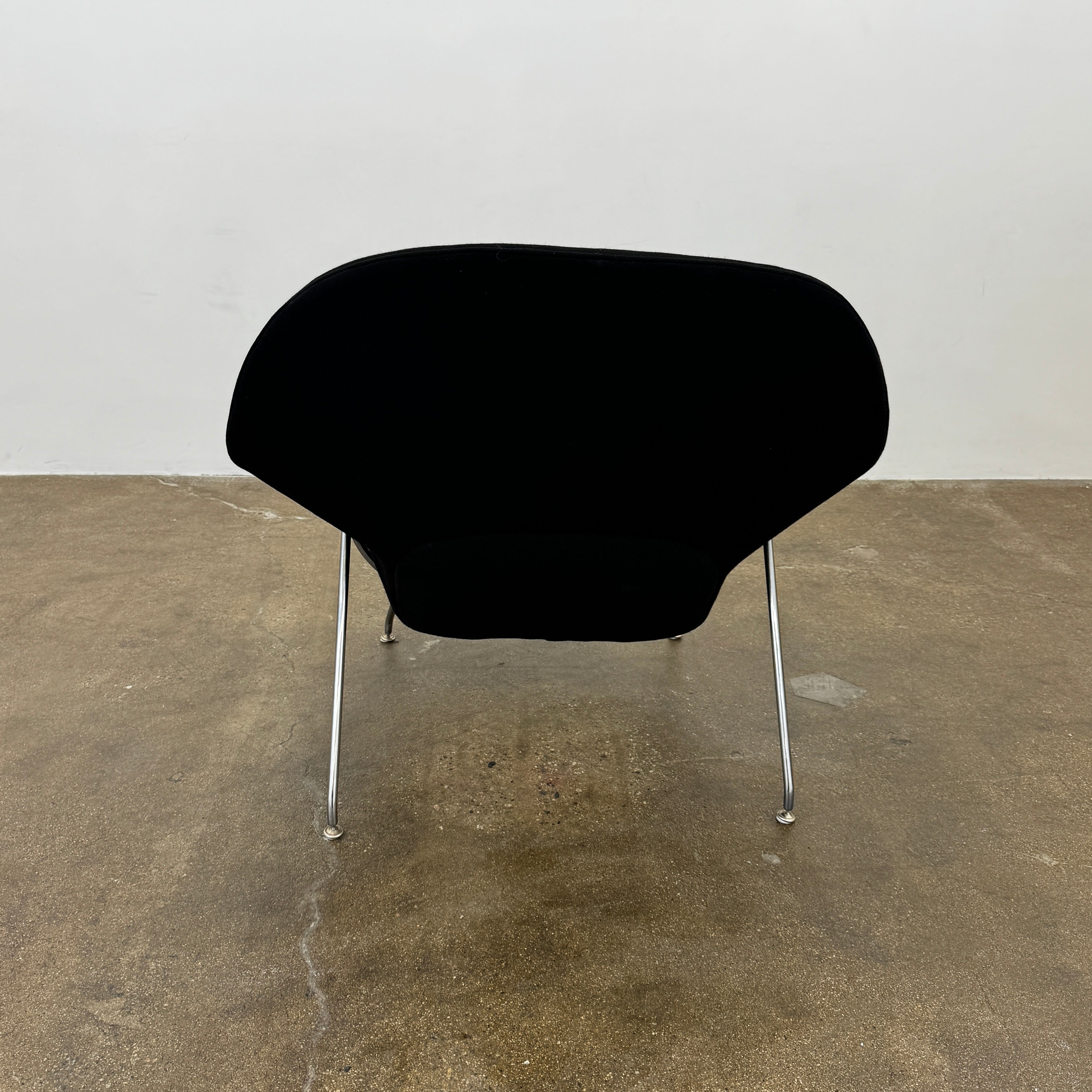 The Knoll Womb Chair by Knoll features a black curved seat, padded cushion, and metal legs, drawing inspiration from midcentury modern design and the iconic Saarinen style. Shown here against a plain white background.