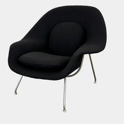 The Knoll Womb Chair by Knoll features a black curved seat, padded cushion, and metal legs, drawing inspiration from midcentury modern design and the iconic Saarinen style. Shown here against a plain white background.