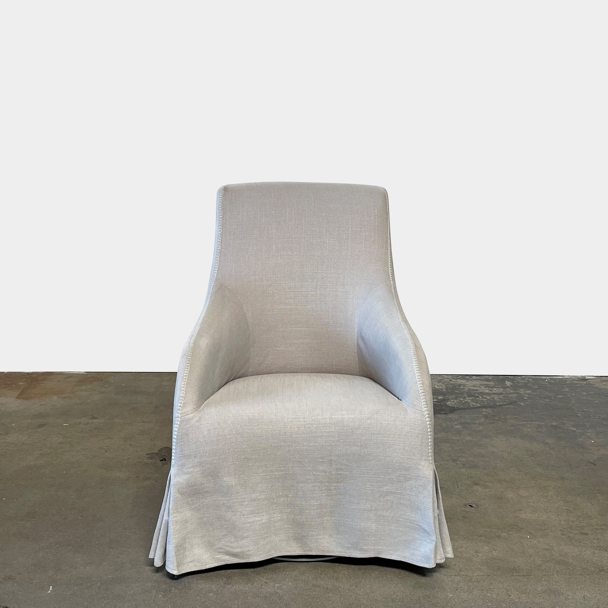 The beige upholstered chair, similar to the Maxalto Agathos Swivel Lounge Chairs, showcases a high back and a skirted bottom against a plain background.