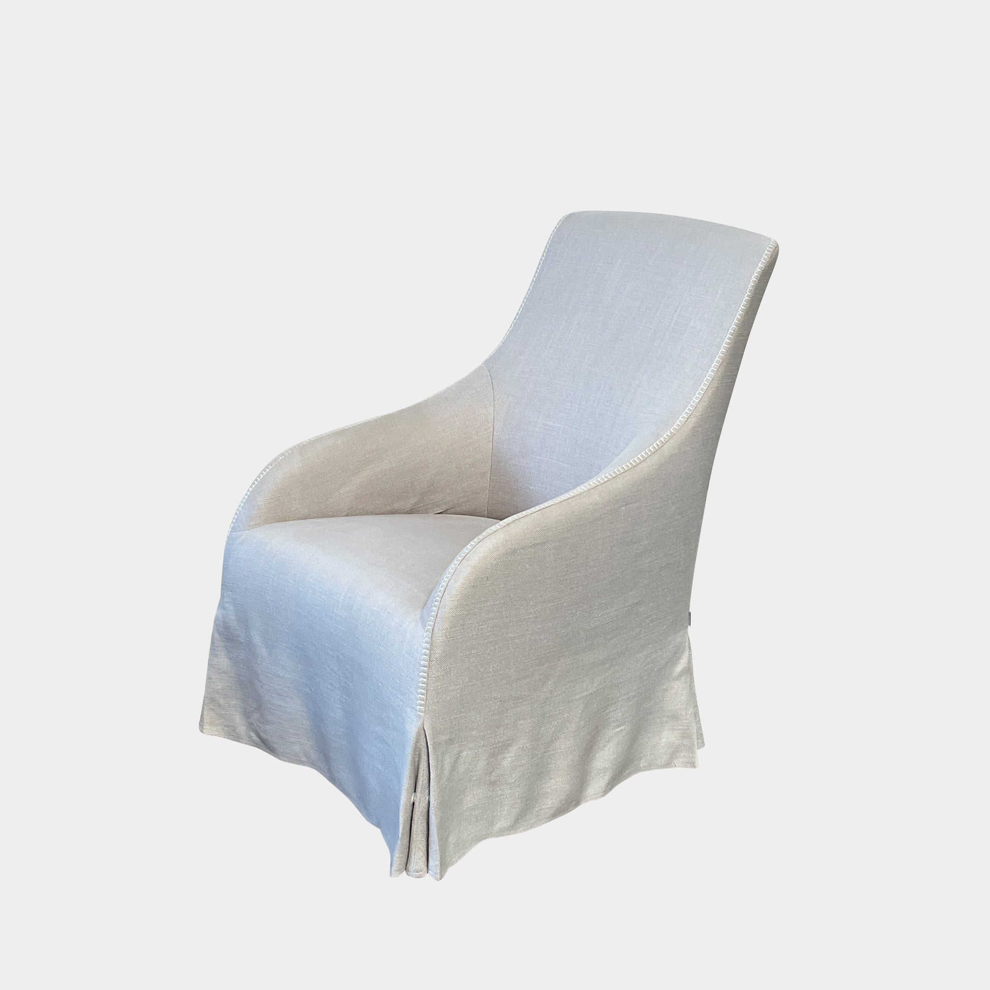 The beige upholstered chair, similar to the Maxalto Agathos Swivel Lounge Chairs, showcases a high back and a skirted bottom against a plain background.