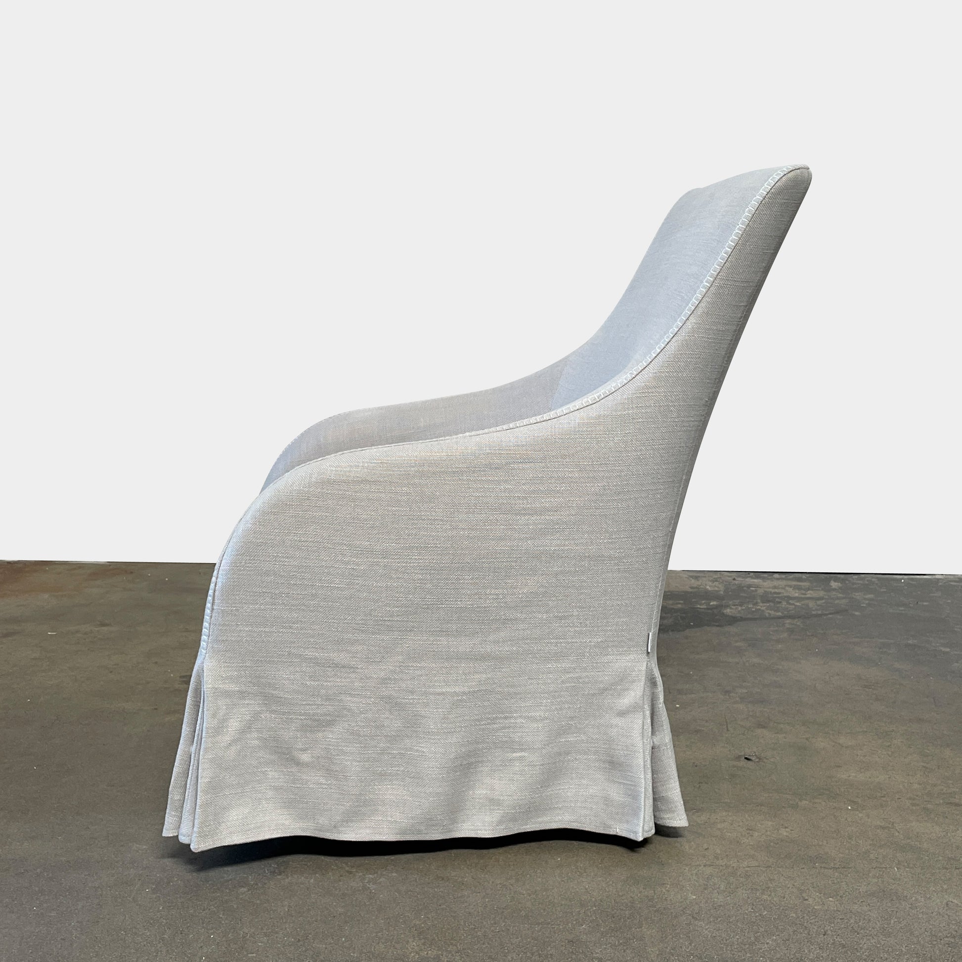 The beige upholstered chair, similar to the Maxalto Agathos Swivel Lounge Chairs, showcases a high back and a skirted bottom against a plain background.