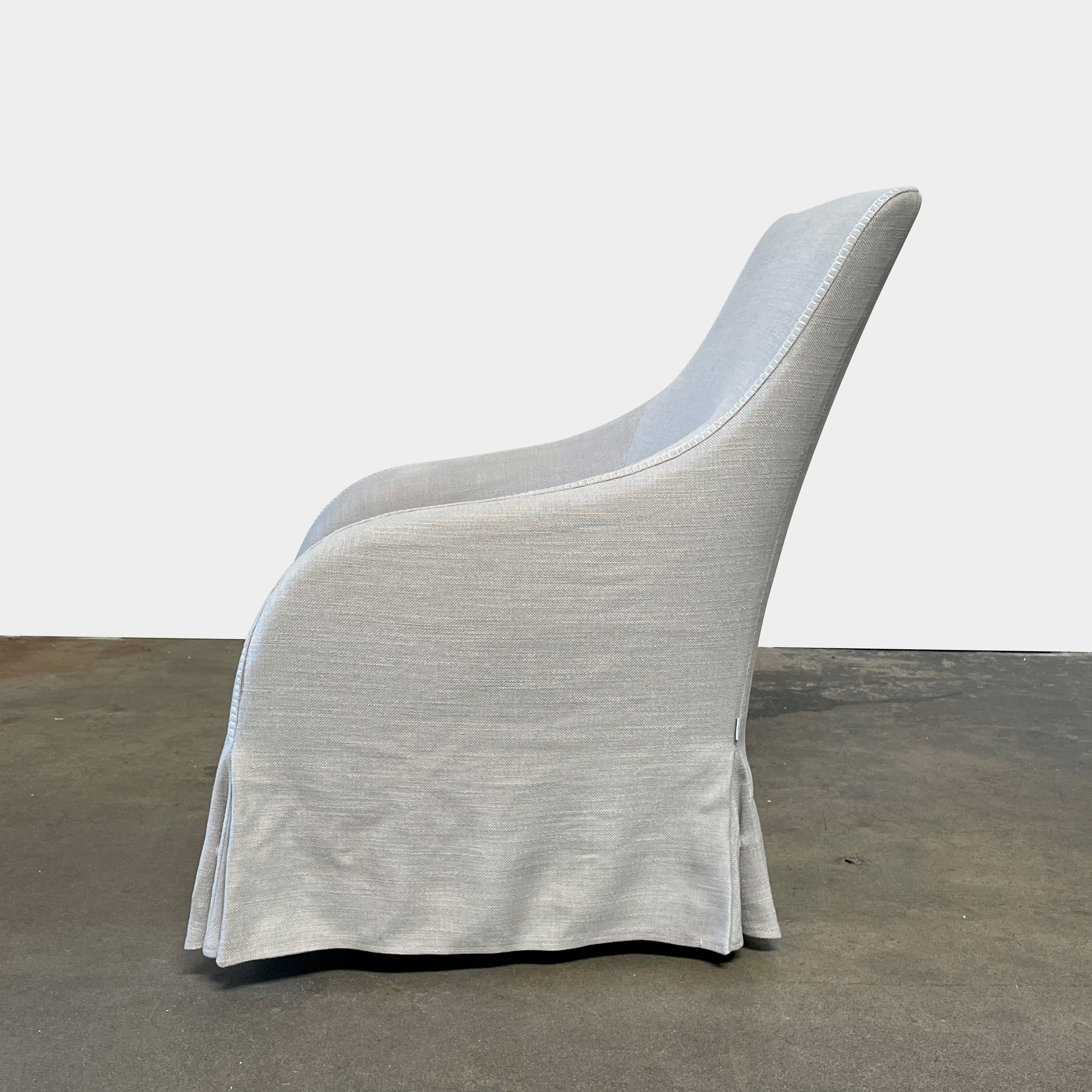 The beige upholstered chair, similar to the Maxalto Agathos Swivel Lounge Chairs, showcases a high back and a skirted bottom against a plain background.