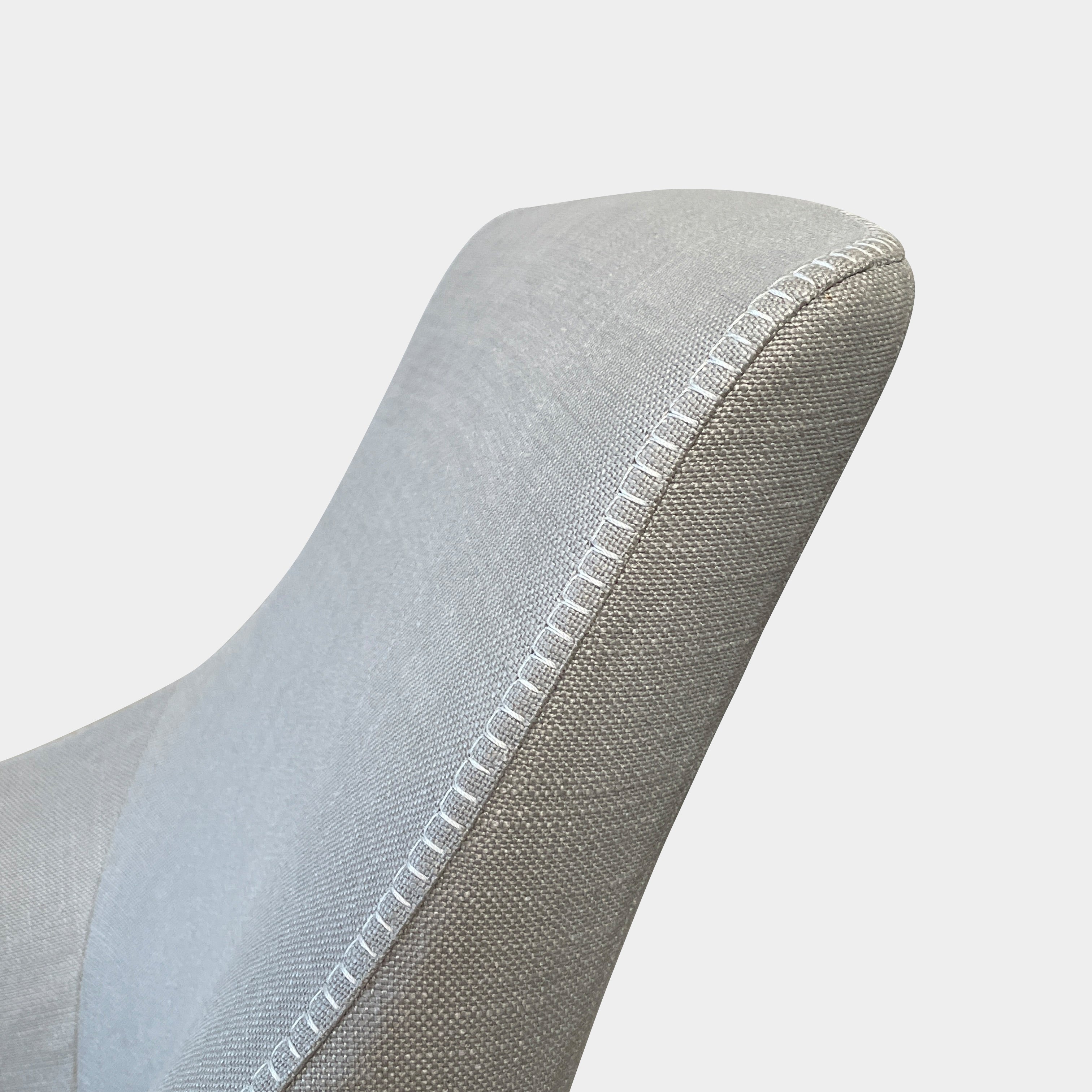 The beige upholstered chair, similar to the Maxalto Agathos Swivel Lounge Chairs, showcases a high back and a skirted bottom against a plain background.