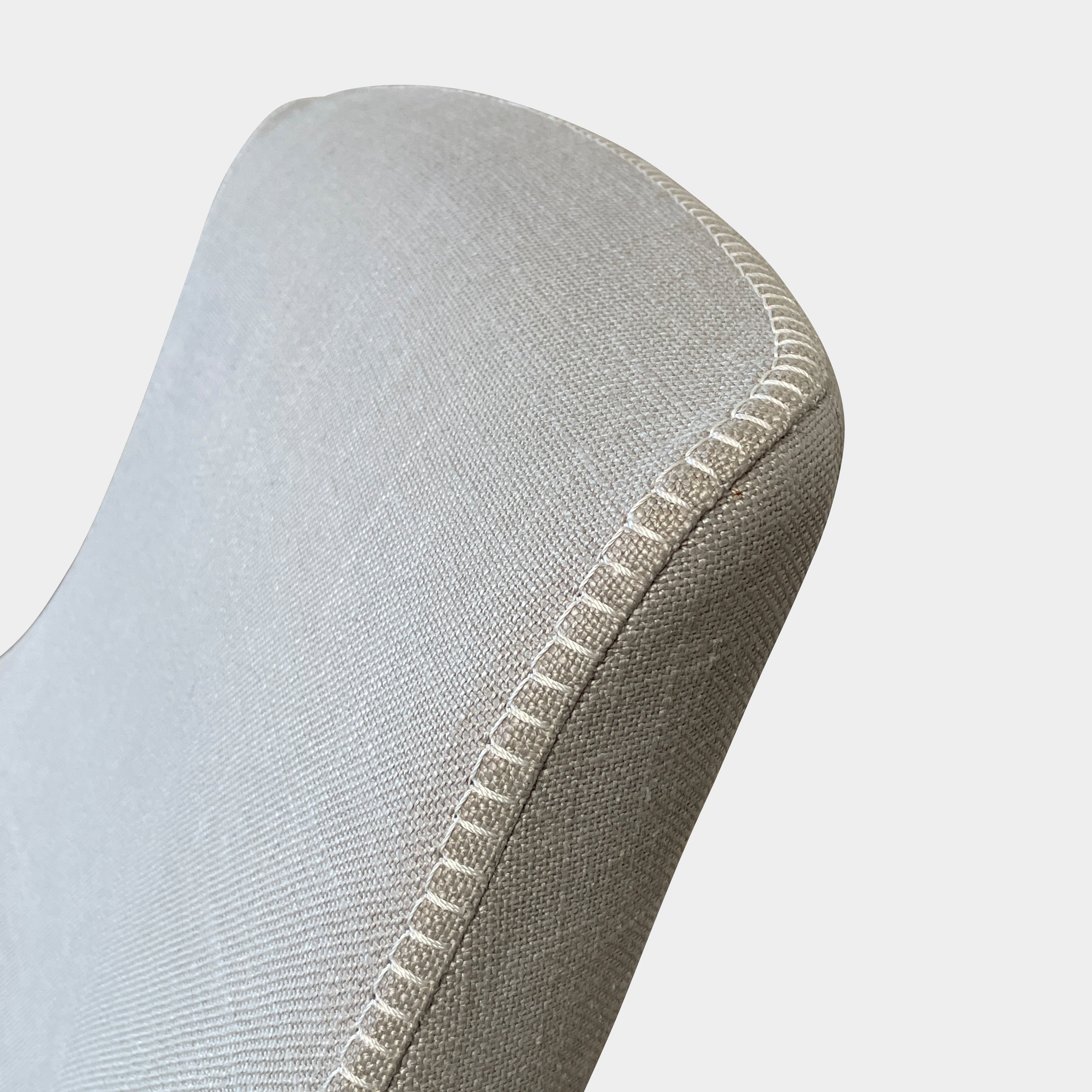 The beige upholstered chair, similar to the Maxalto Agathos Swivel Lounge Chairs, showcases a high back and a skirted bottom against a plain background.