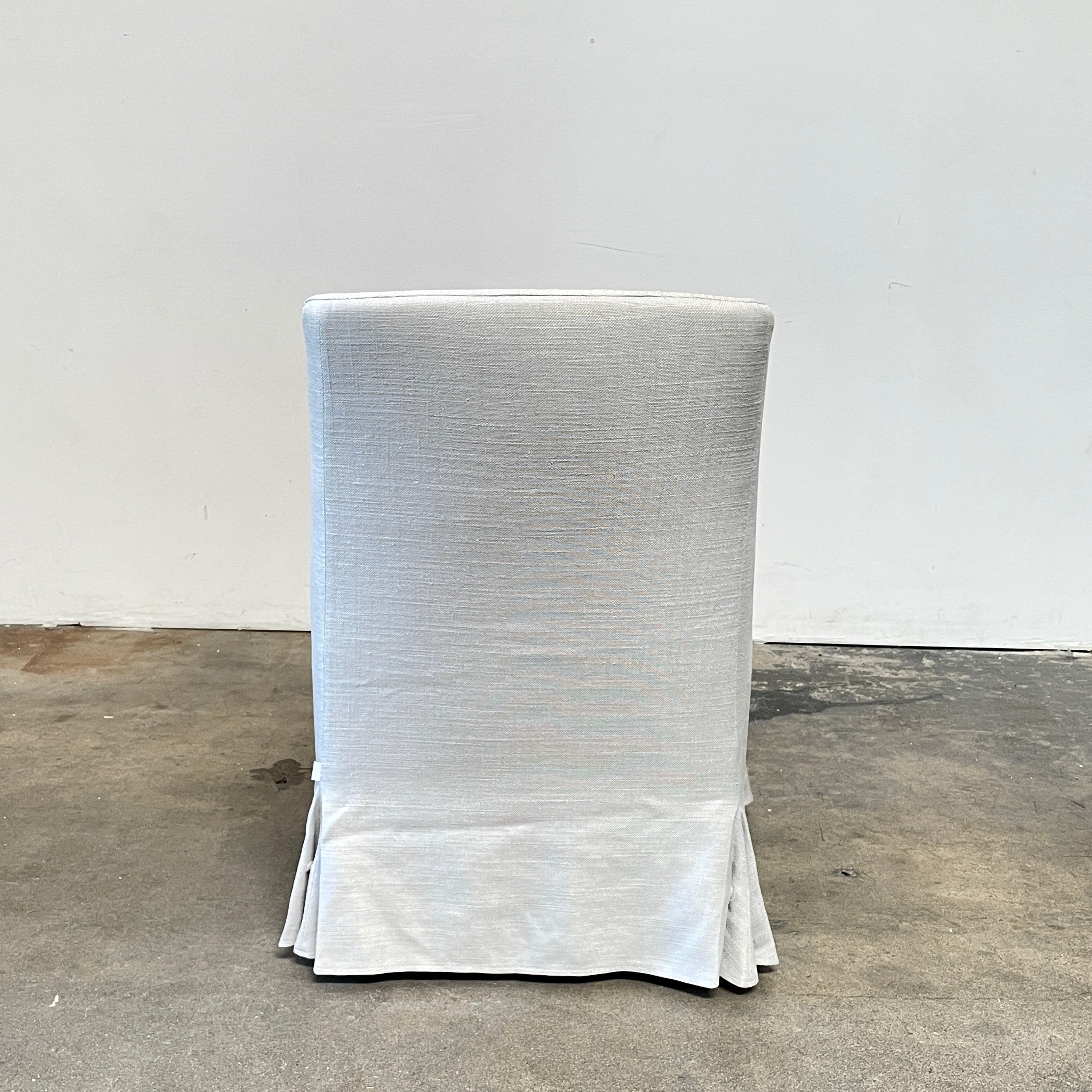 The beige upholstered chair, similar to the Maxalto Agathos Swivel Lounge Chairs, showcases a high back and a skirted bottom against a plain background.