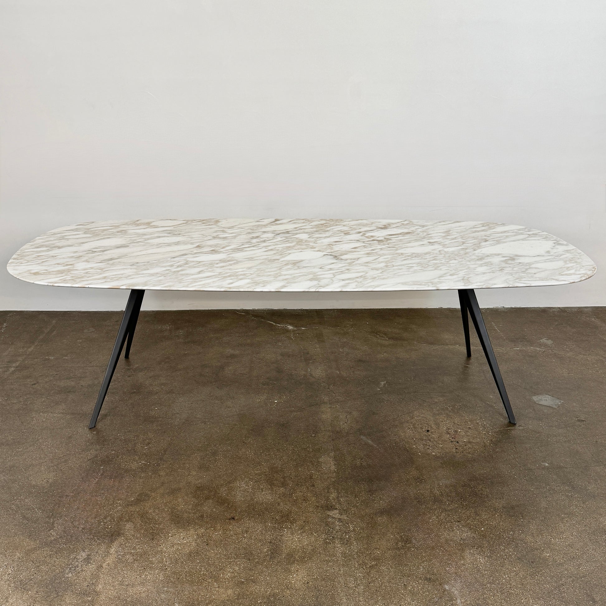 The Flexform Zefiro Dining Table by Flexform features a rectangular Calacatta Gold marble top with rounded edges and four black angled legs, shown on a plain white background.