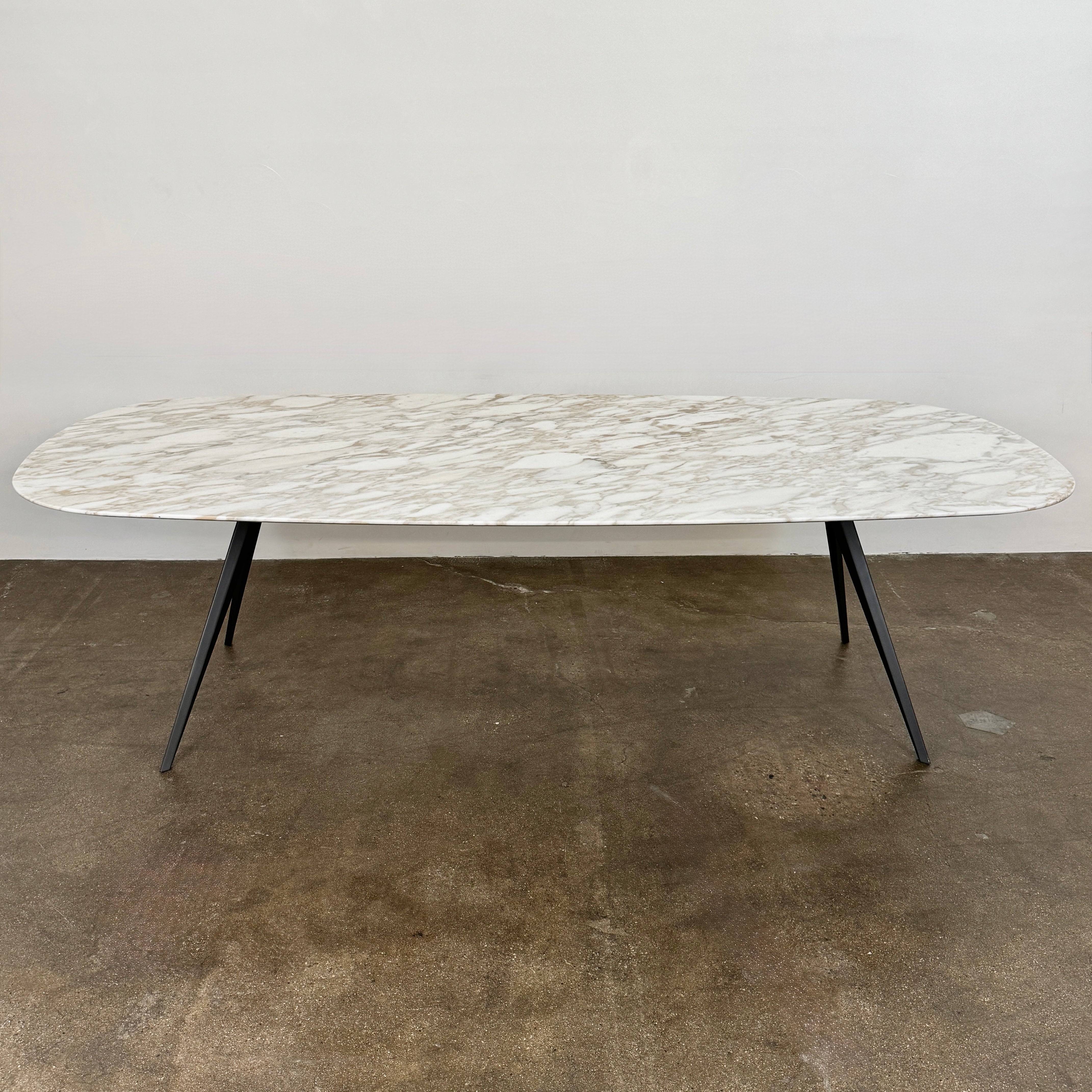 The Flexform Zefiro Dining Table by Flexform features a rectangular Calacatta Gold marble top with rounded edges and four black angled legs, shown on a plain white background.