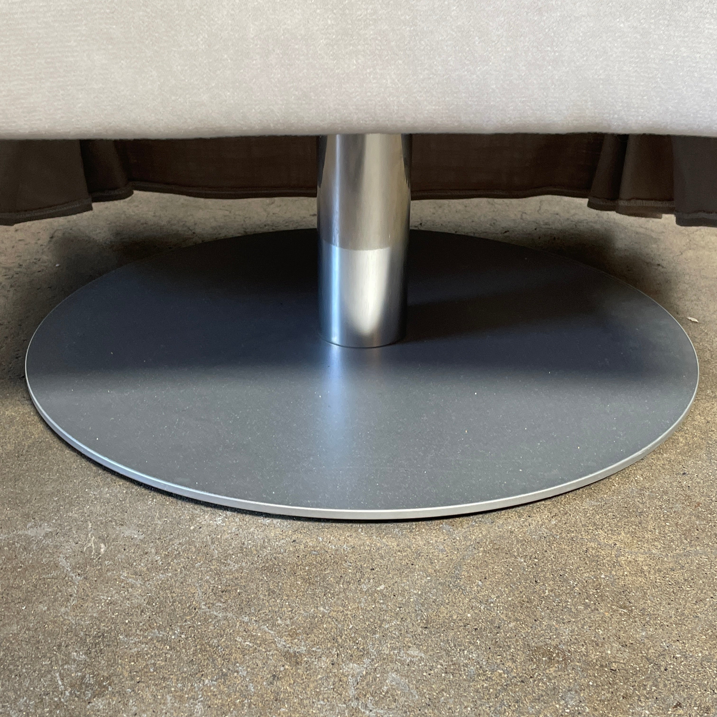 The beige upholstered chair, similar to the Maxalto Agathos Swivel Lounge Chairs, showcases a high back and a skirted bottom against a plain background.