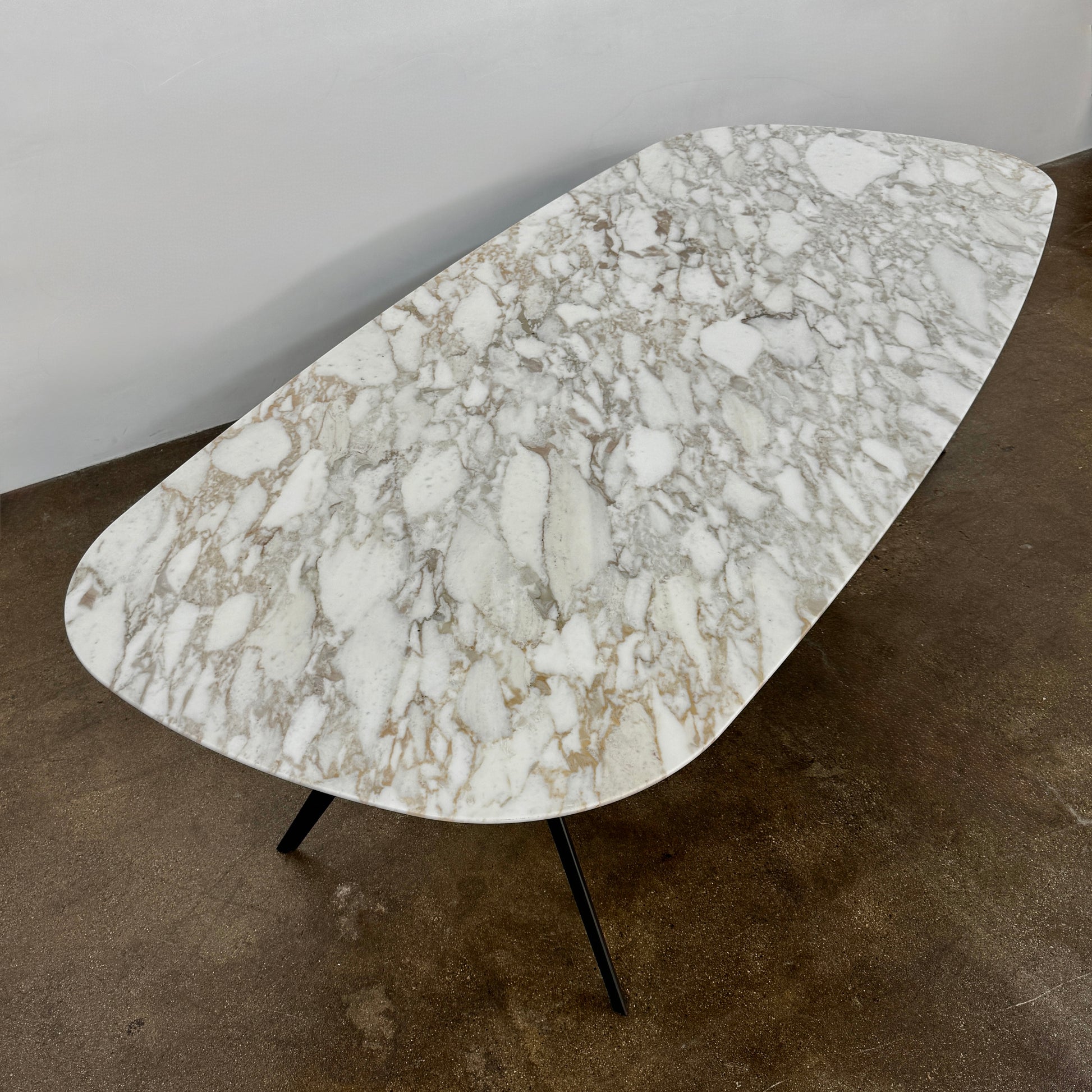 The Flexform Zefiro Dining Table by Flexform features a rectangular Calacatta Gold marble top with rounded edges and four black angled legs, shown on a plain white background.