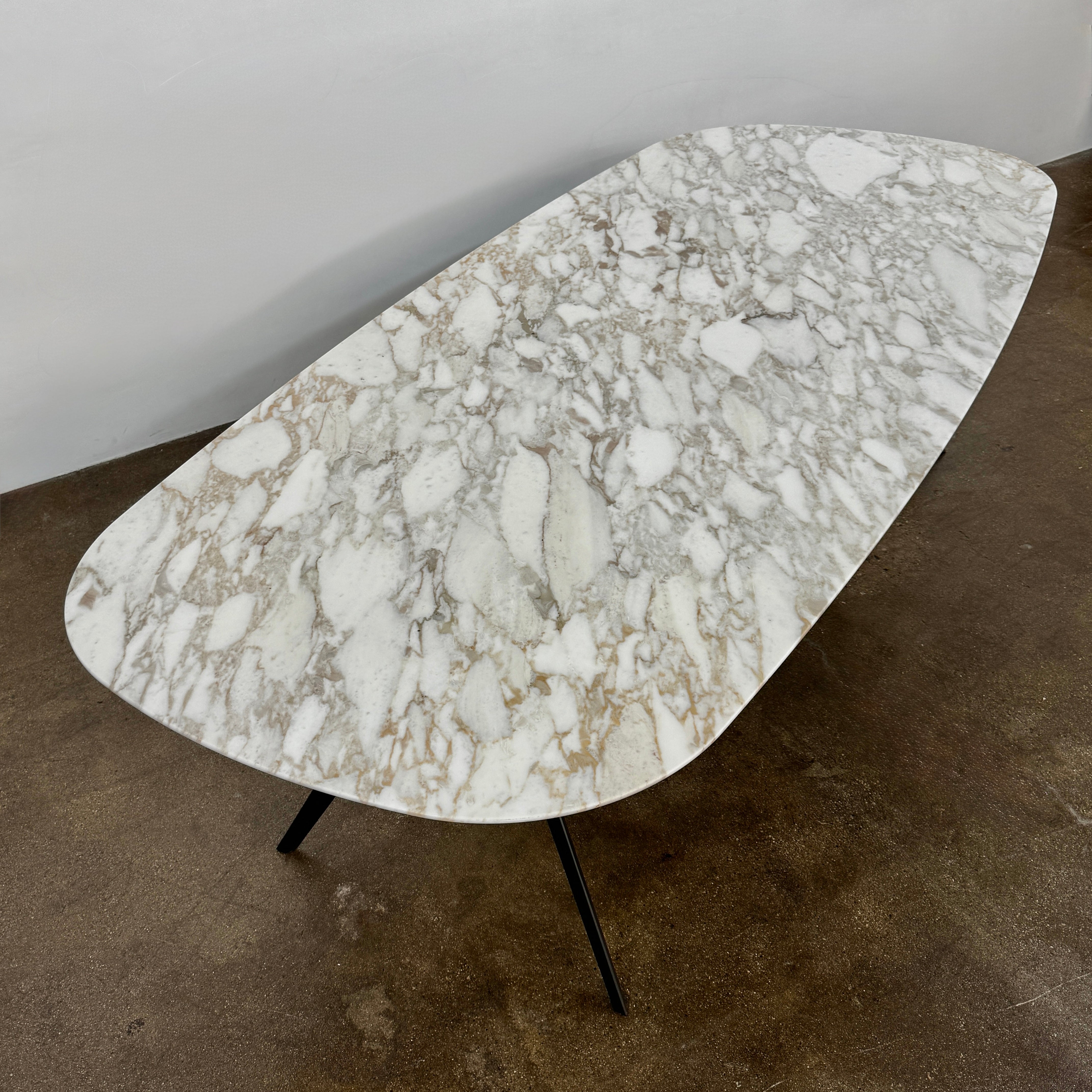 The Flexform Zefiro Dining Table by Flexform features a rectangular Calacatta Gold marble top with rounded edges and four black angled legs, shown on a plain white background.