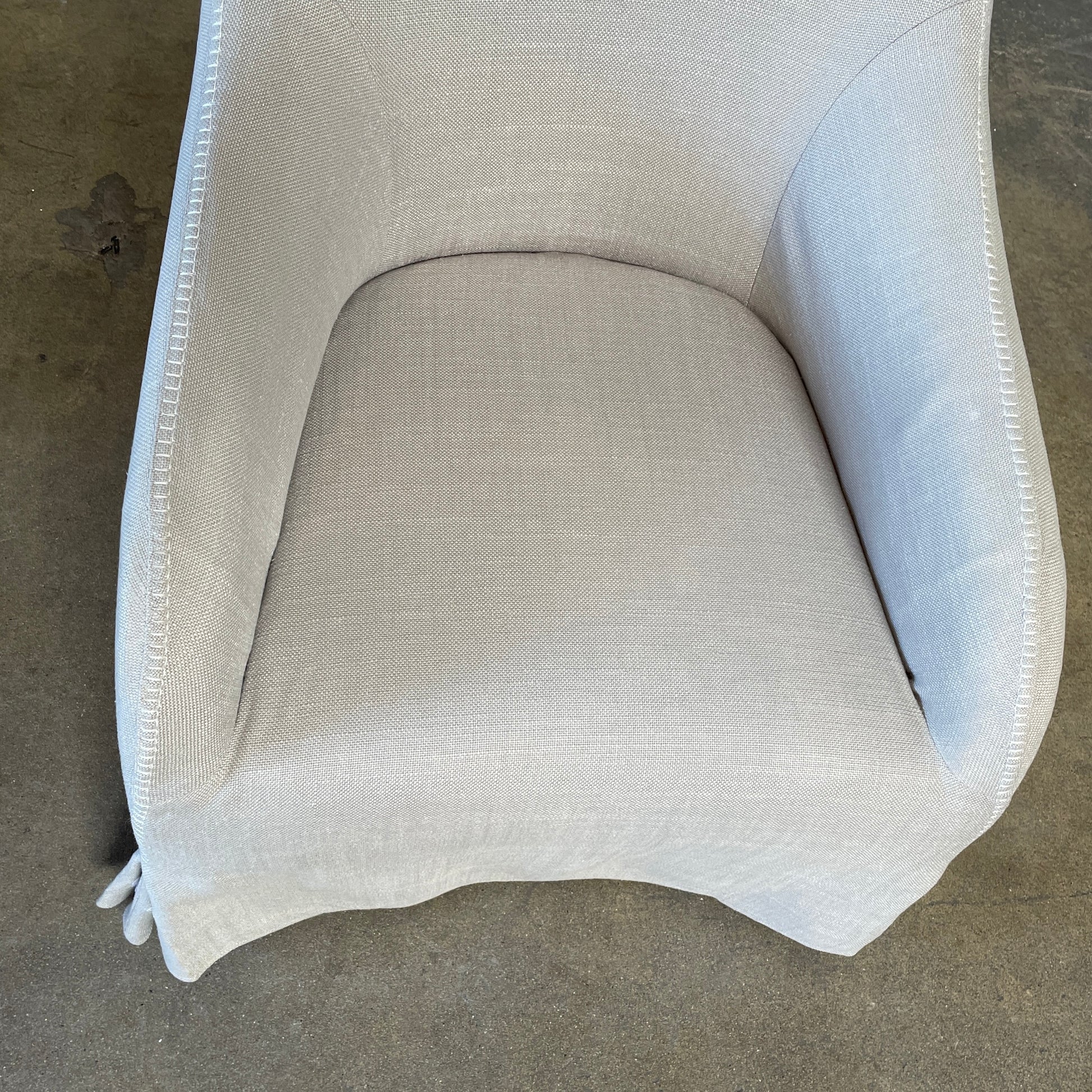 The beige upholstered chair, similar to the Maxalto Agathos Swivel Lounge Chairs, showcases a high back and a skirted bottom against a plain background.