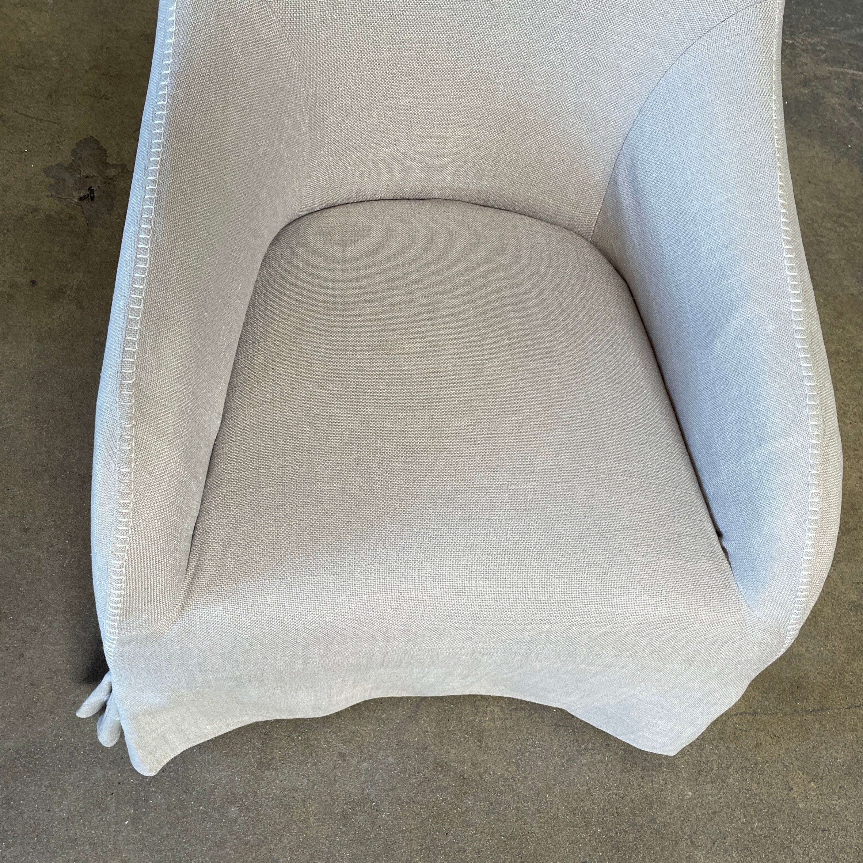 The beige upholstered chair, similar to the Maxalto Agathos Swivel Lounge Chairs, showcases a high back and a skirted bottom against a plain background.