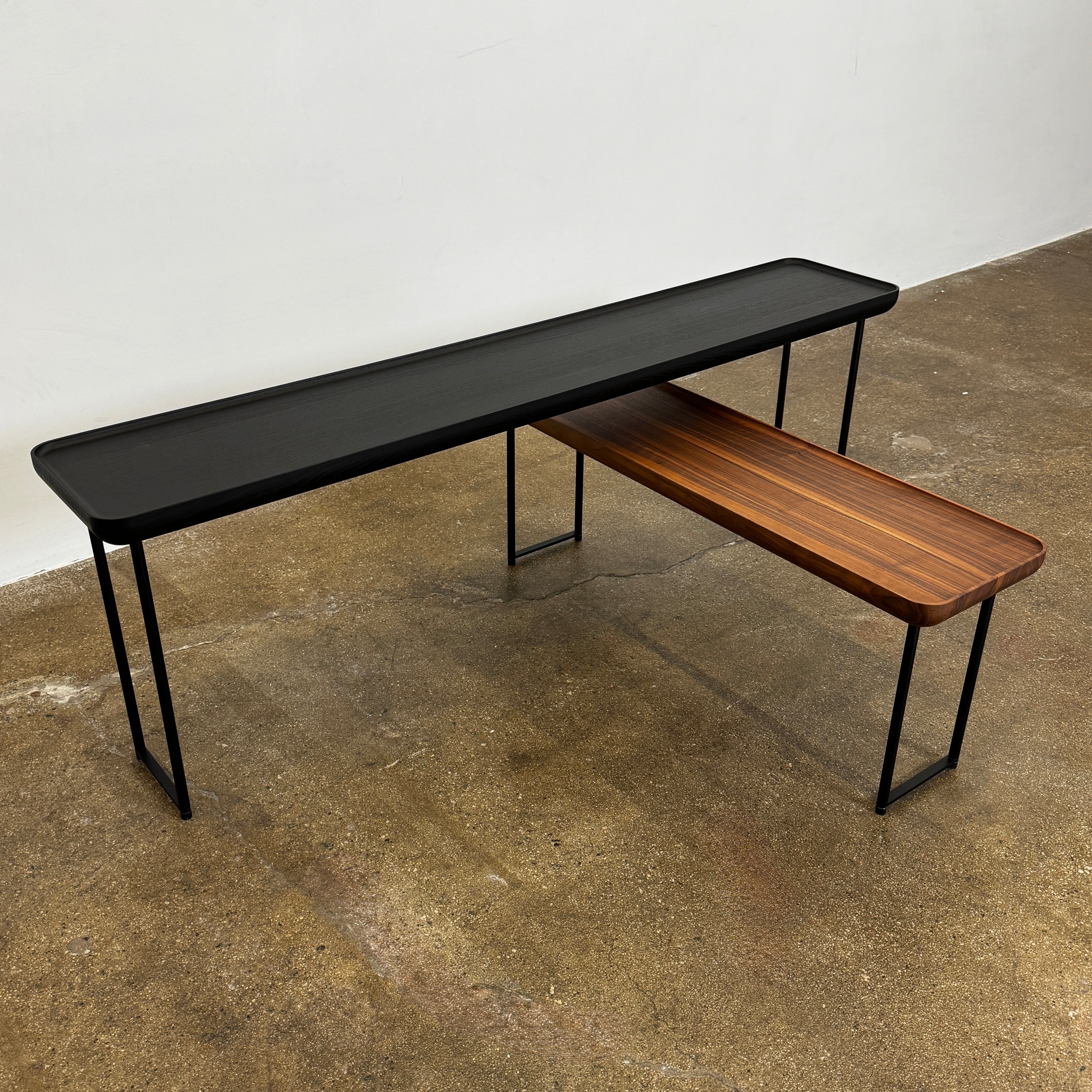 A minimalist black bench with a rectangular seat and slim metal legs echoes the elegant design of the Cassina Torei Occasional Table in Black Ash by Cassina, displayed against a plain white background.