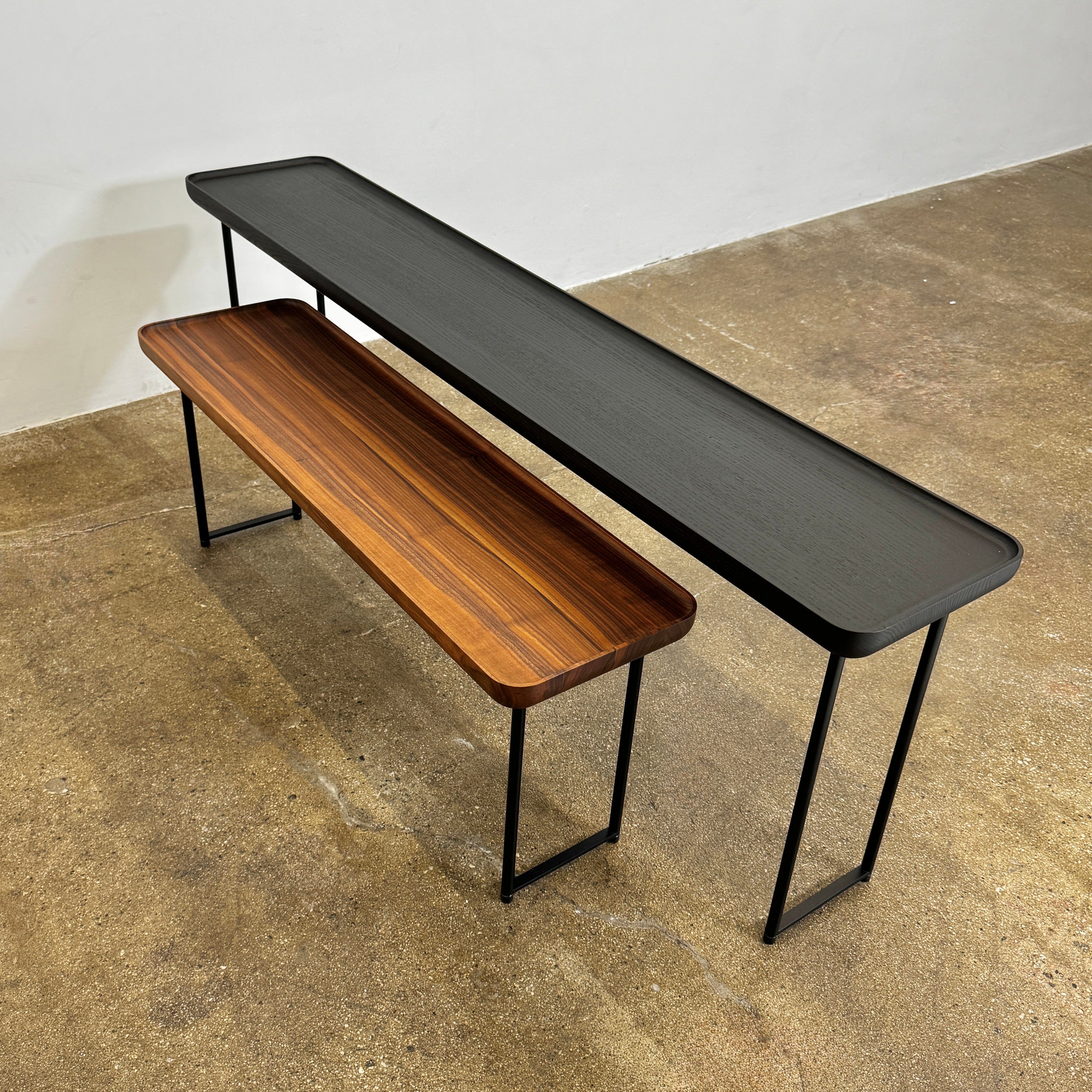 A minimalist black bench with a rectangular seat and slim metal legs echoes the elegant design of the Cassina Torei Occasional Table in Black Ash by Cassina, displayed against a plain white background.