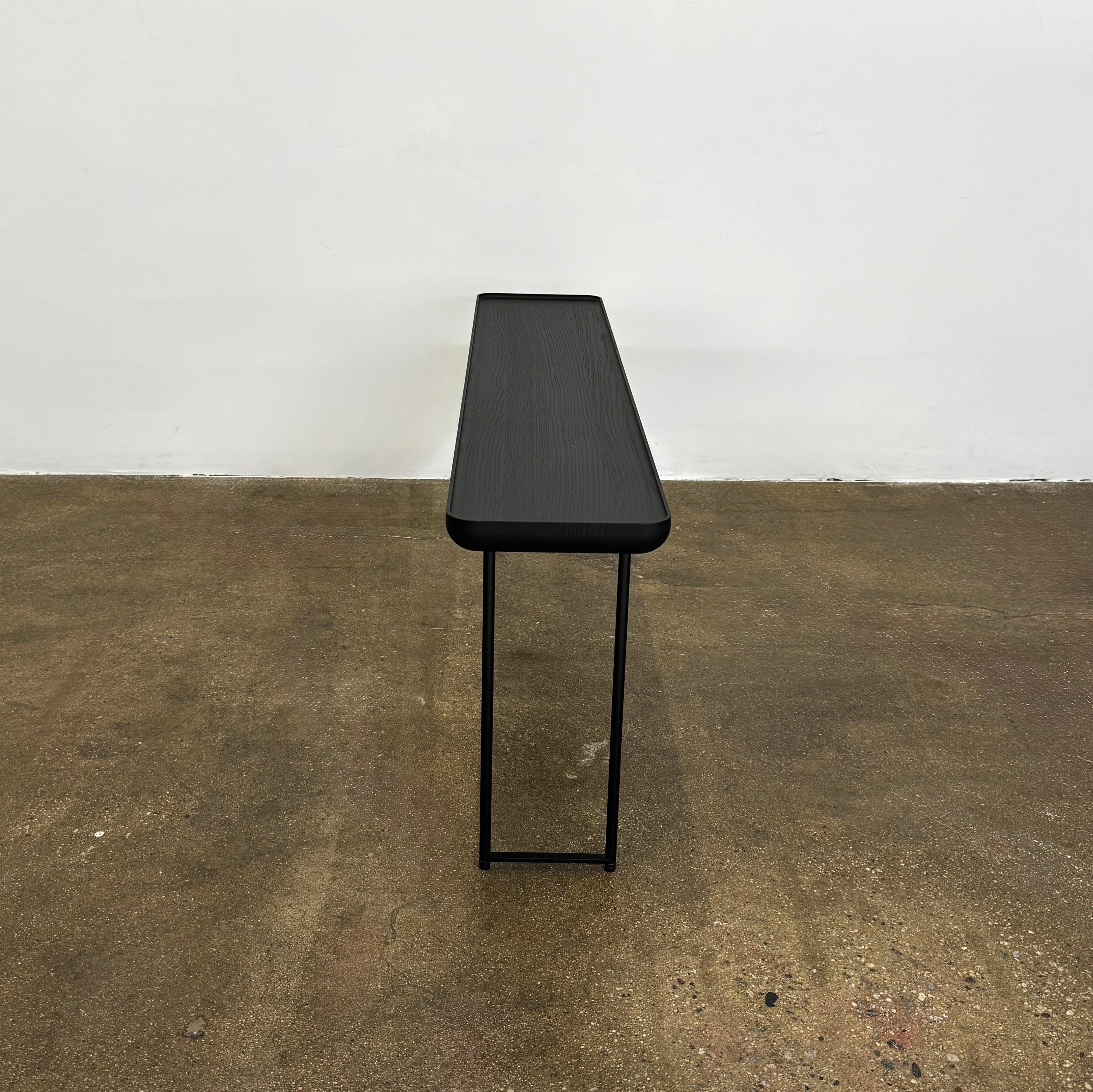 A minimalist black bench with a rectangular seat and slim metal legs echoes the elegant design of the Cassina Torei Occasional Table in Black Ash by Cassina, displayed against a plain white background.
