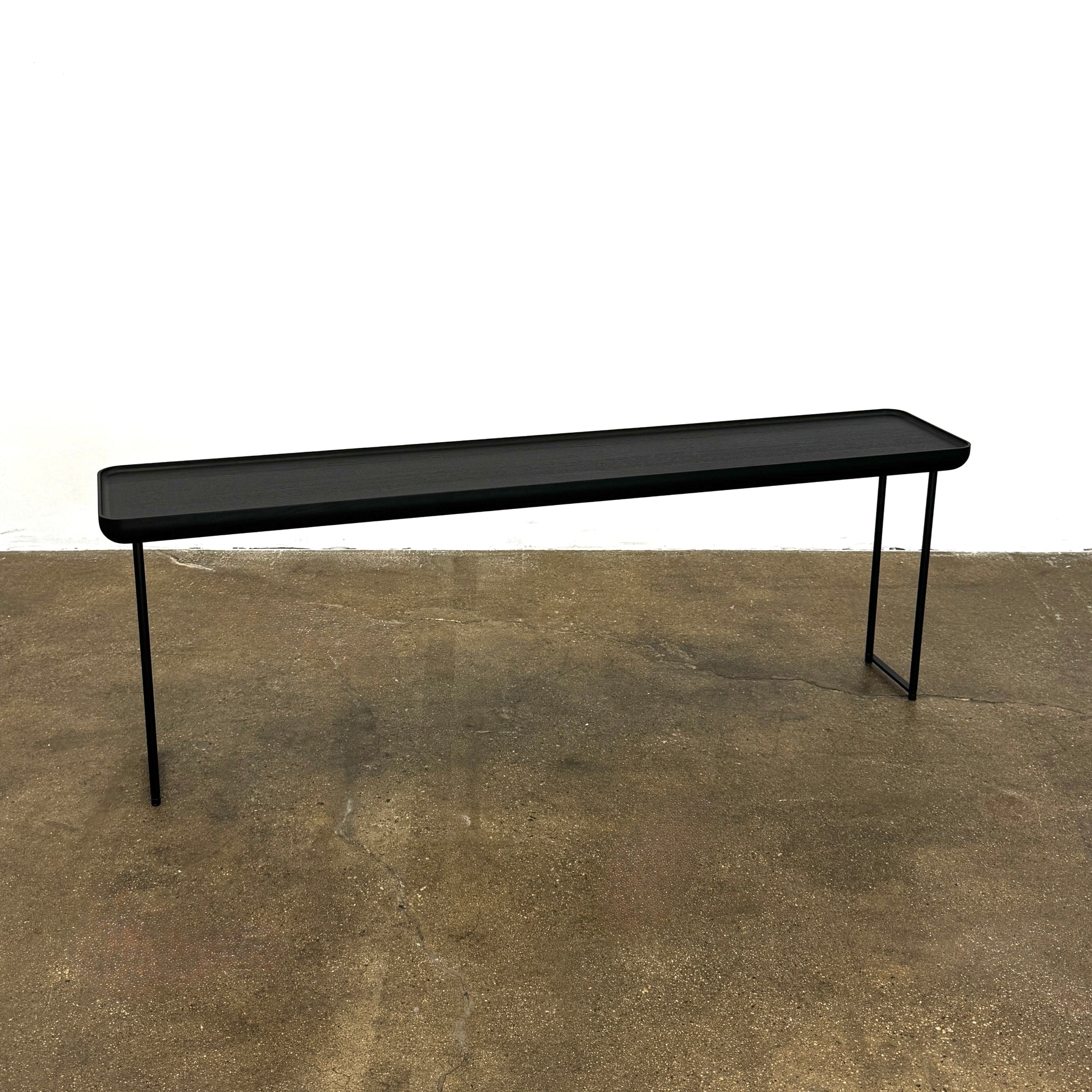 A minimalist black bench with a rectangular seat and slim metal legs echoes the elegant design of the Cassina Torei Occasional Table in Black Ash by Cassina, displayed against a plain white background.
