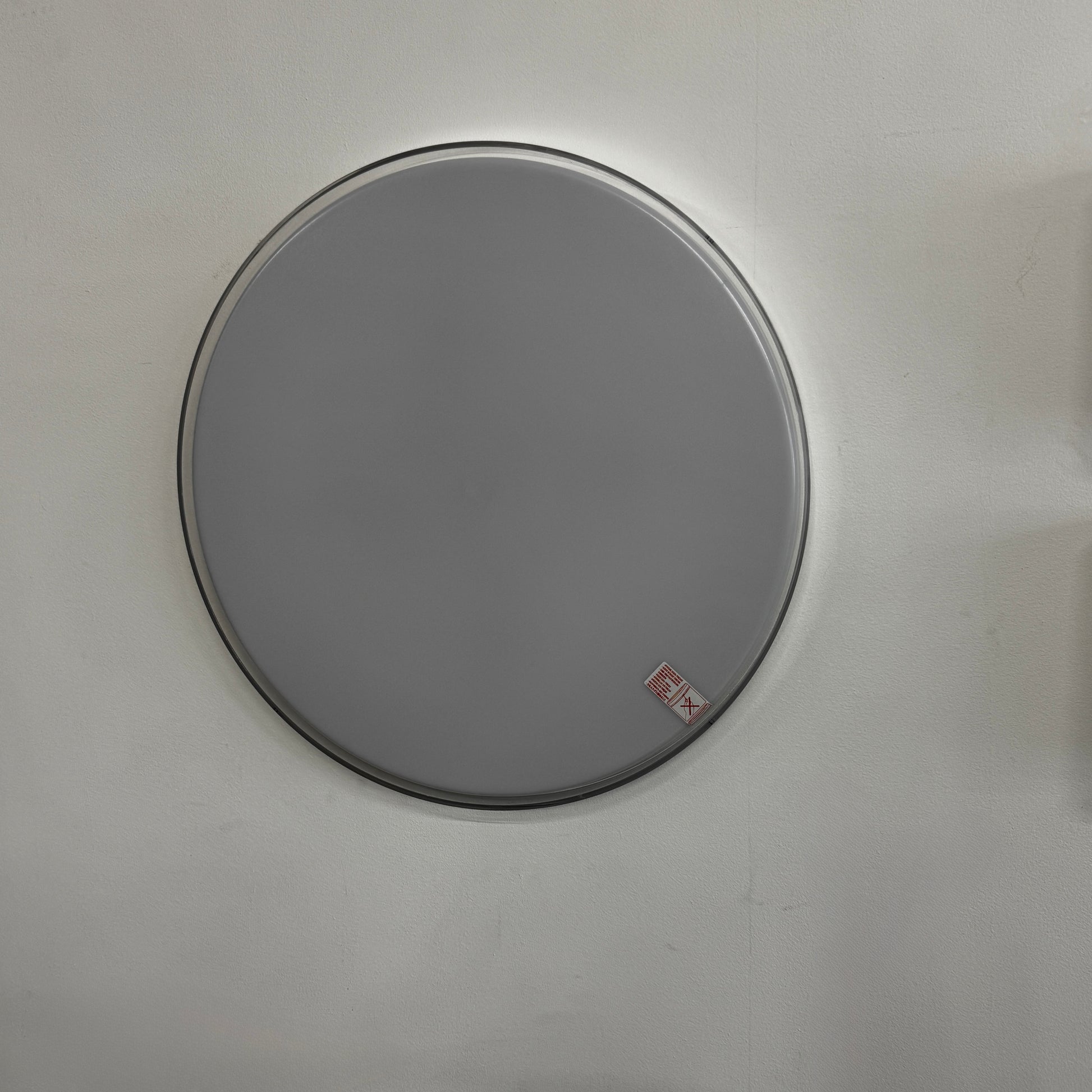 A round, frameless mirror is mounted on a light gray wall, complemented by the Flos Clara Flush-mounted Wall Ceiling LED Light, enhancing the clean and minimalist aesthetic.