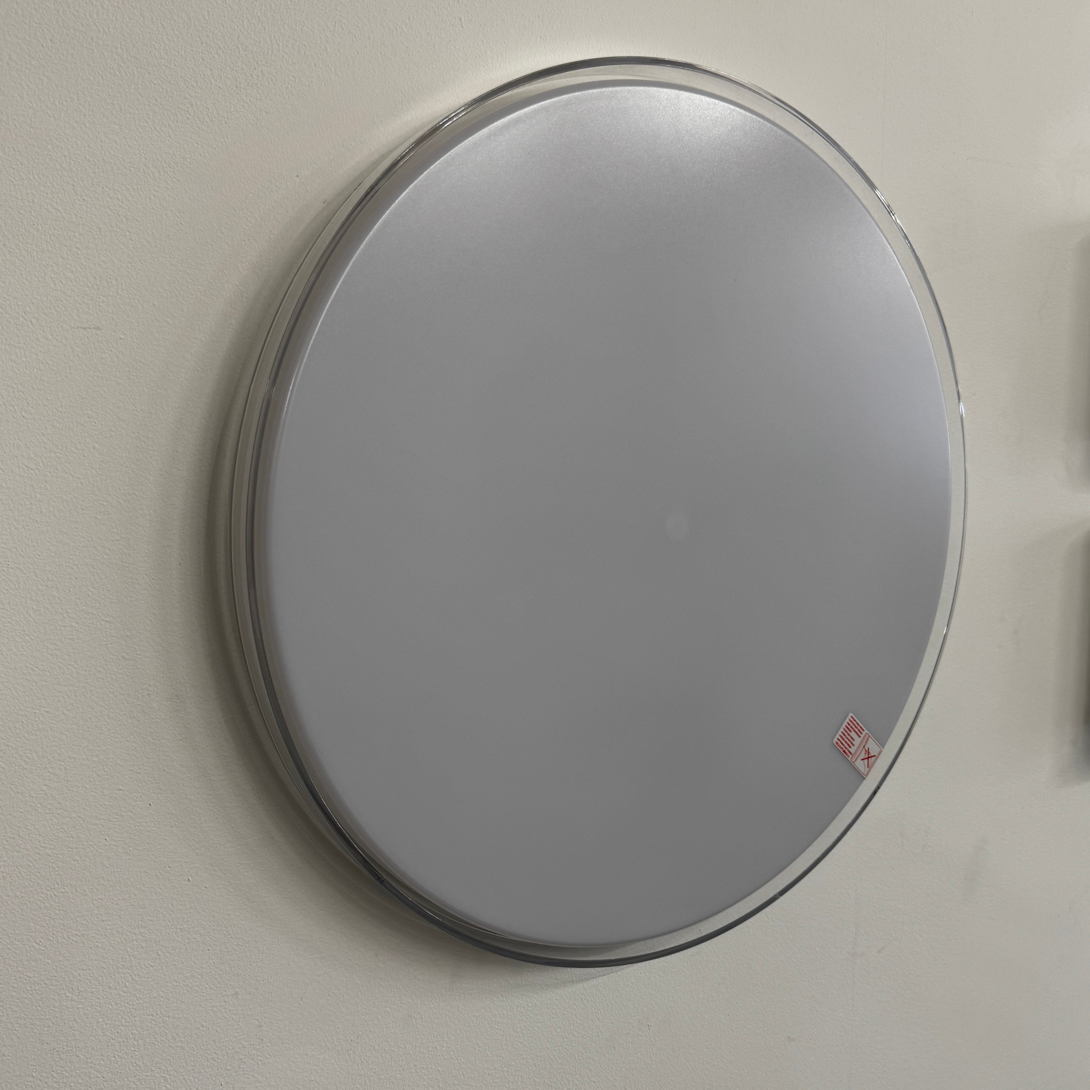 A round, frameless mirror is mounted on a light gray wall, complemented by the Flos Clara Flush-mounted Wall Ceiling LED Light, enhancing the clean and minimalist aesthetic.