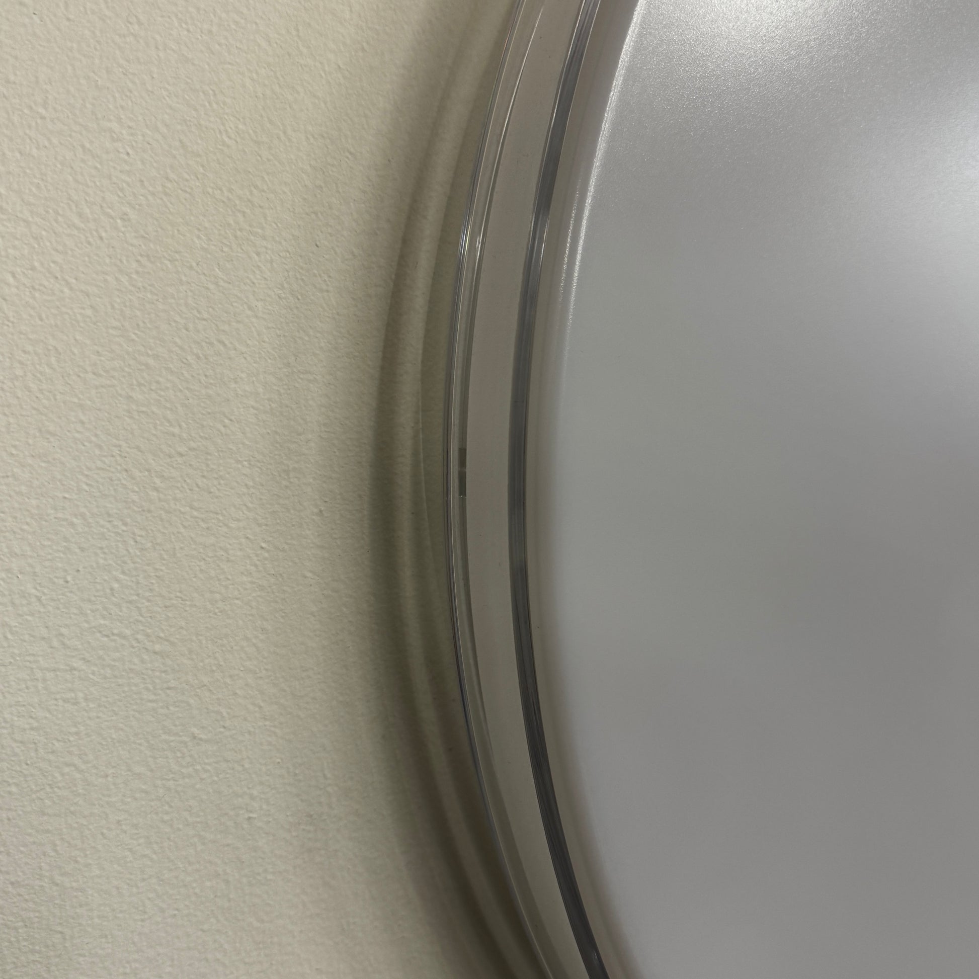 A round, frameless mirror is mounted on a light gray wall, complemented by the Flos Clara Flush-mounted Wall Ceiling LED Light, enhancing the clean and minimalist aesthetic.