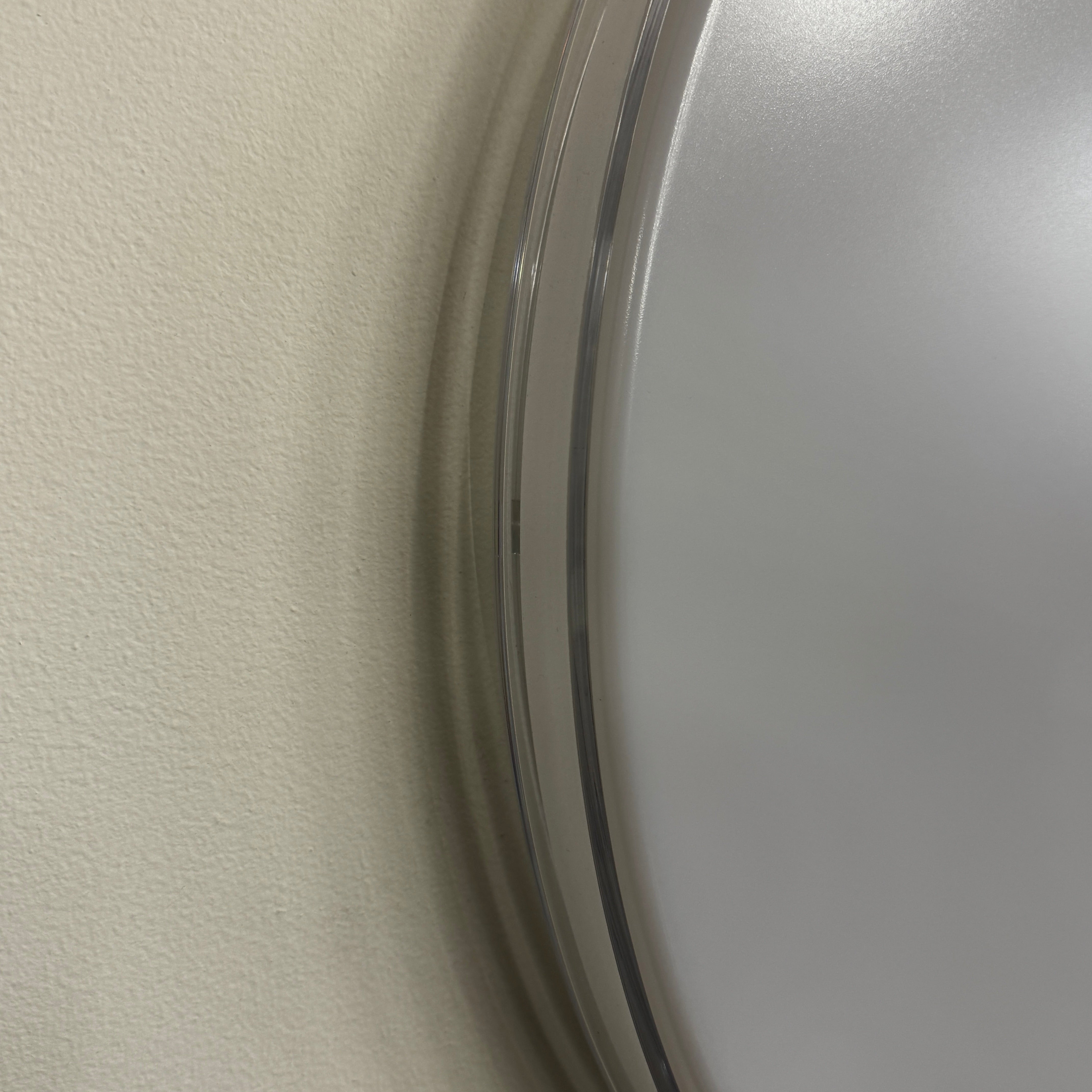 A round, frameless mirror is mounted on a light gray wall, complemented by the Flos Clara Flush-mounted Wall Ceiling LED Light, enhancing the clean and minimalist aesthetic.
