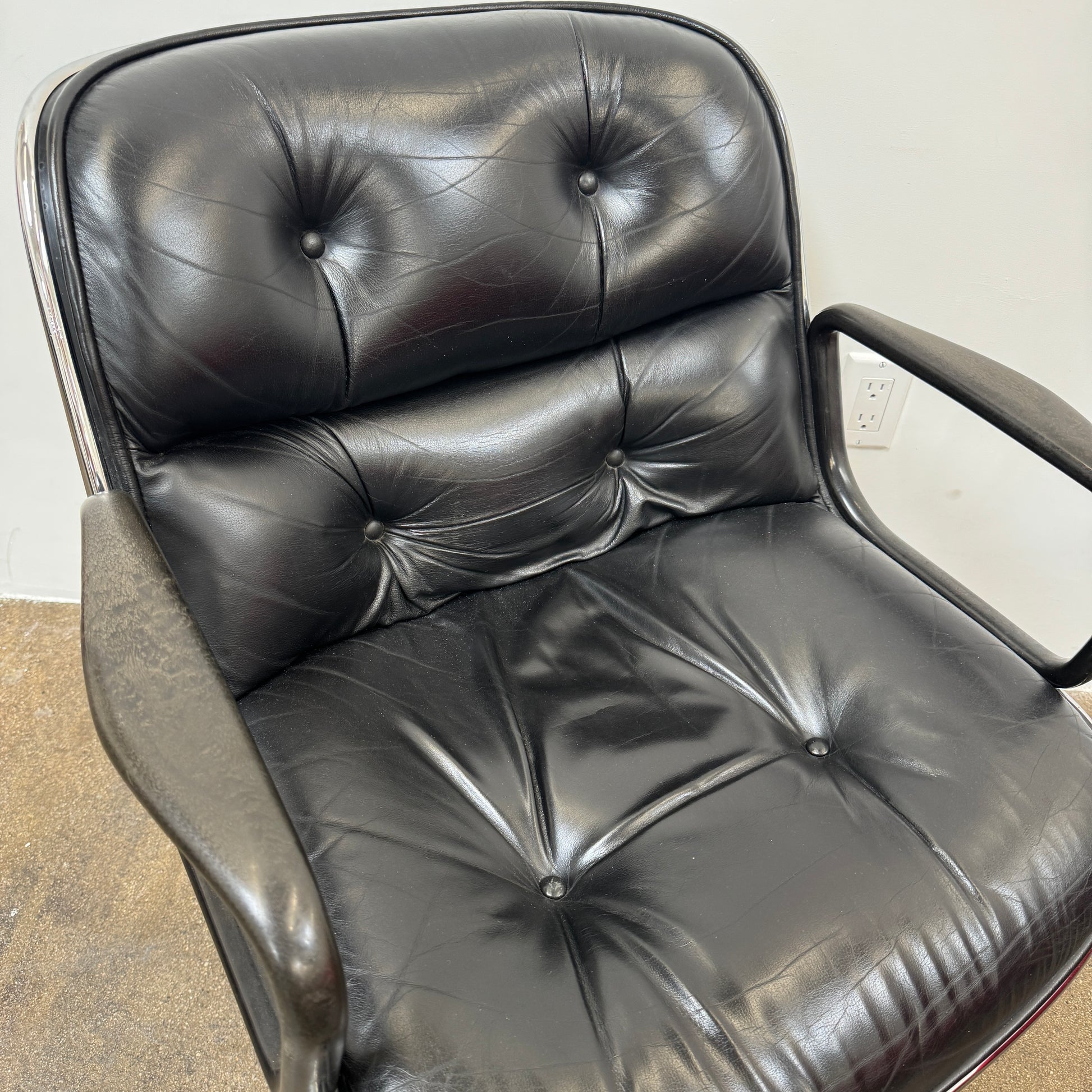 A DWR Pollock Executive Chair with a chrome frame and five wheels is shown from the back, set on a concrete floor against a plain white wall.