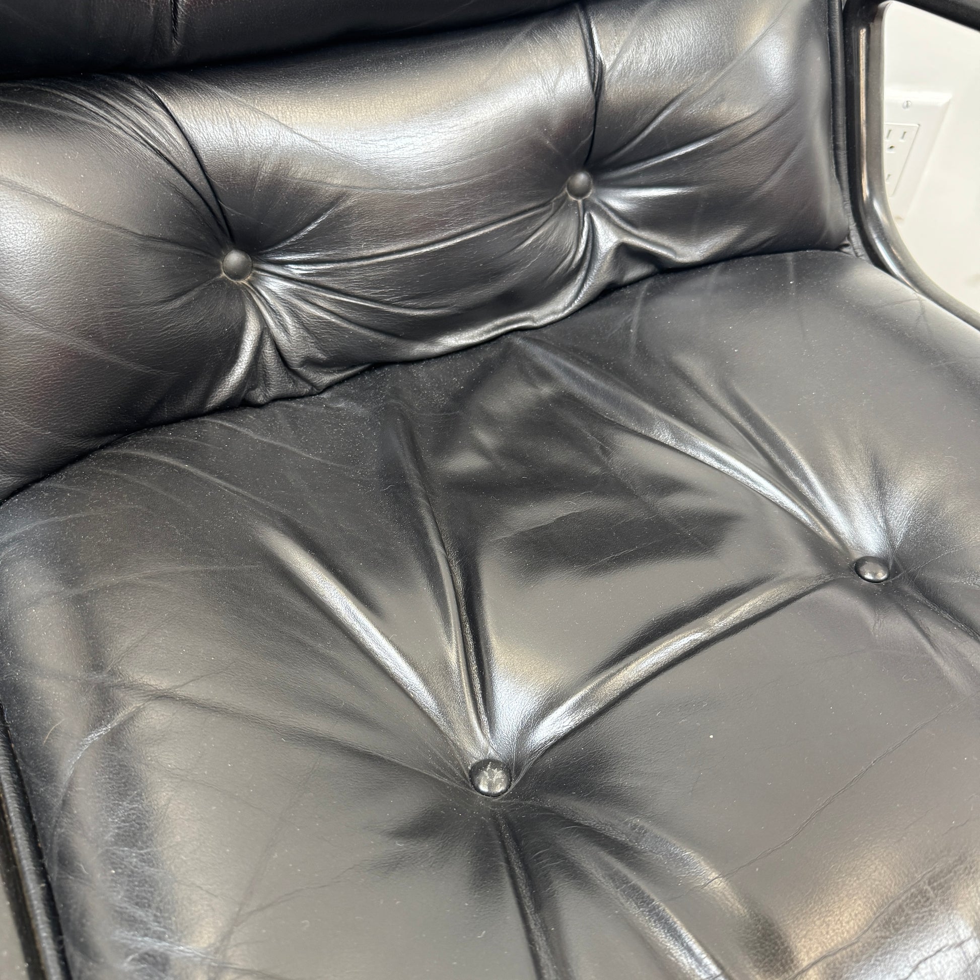 A DWR Pollock Executive Chair with a chrome frame and five wheels is shown from the back, set on a concrete floor against a plain white wall.