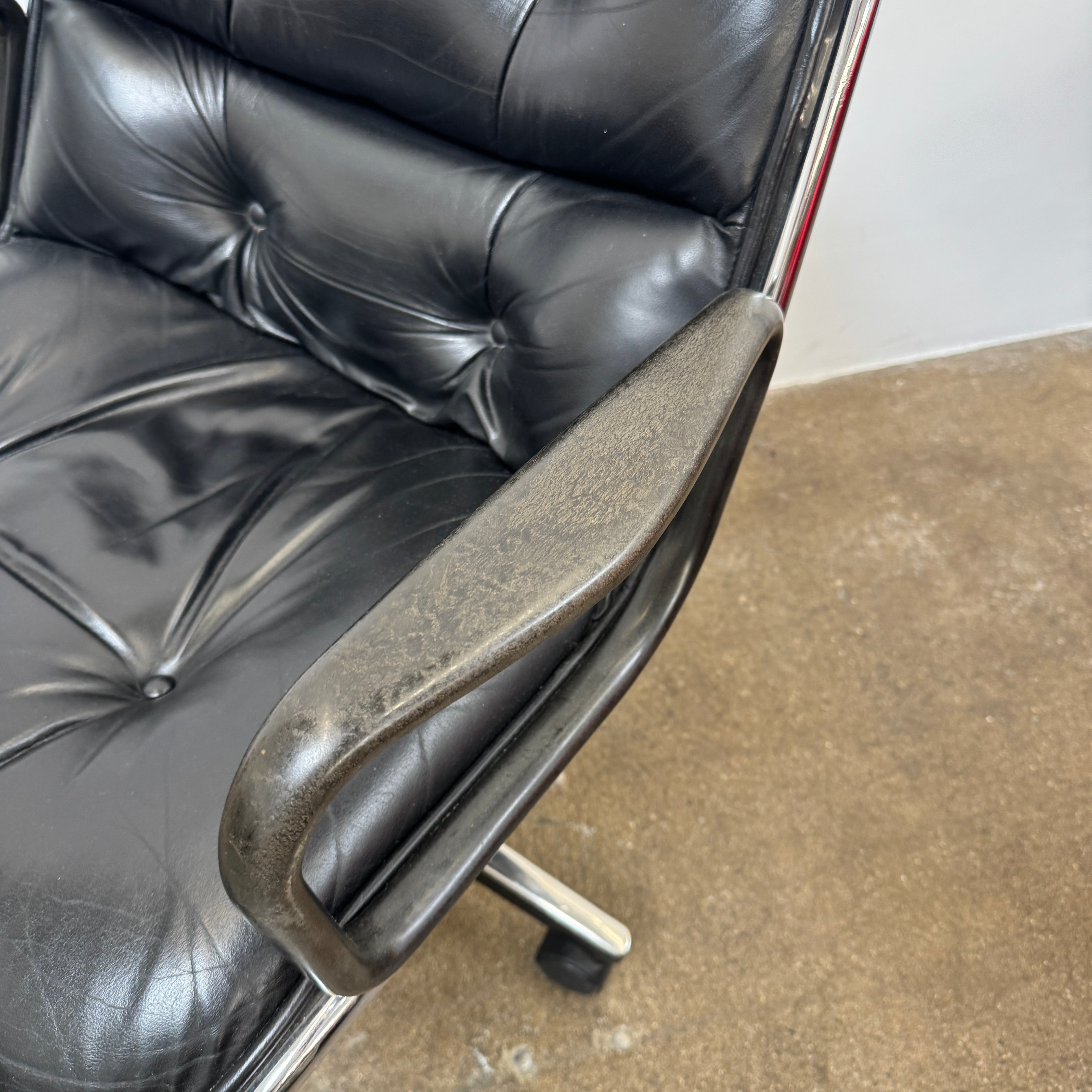 A DWR Pollock Executive Chair with a chrome frame and five wheels is shown from the back, set on a concrete floor against a plain white wall.