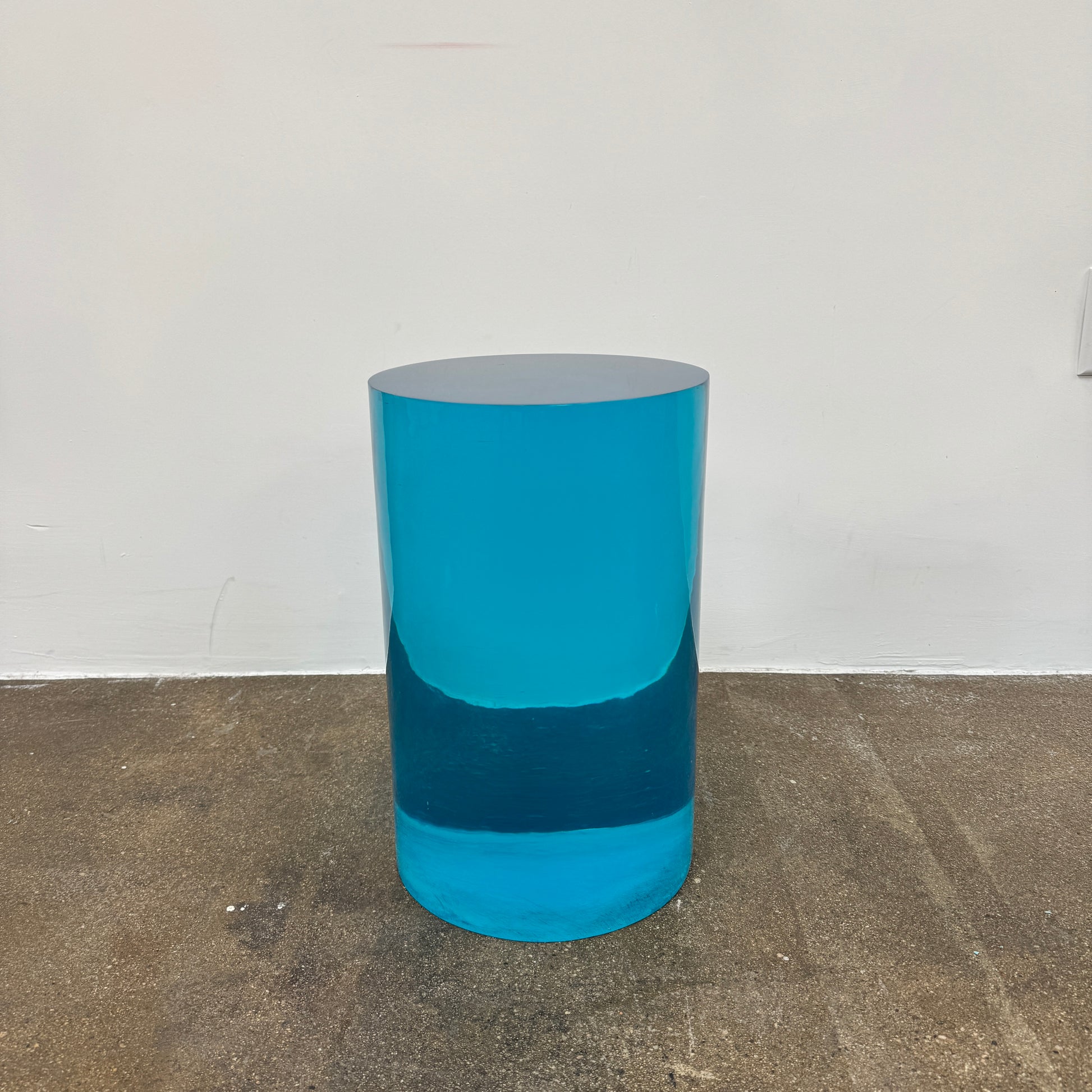 The Jonathan Adler blue acrylic cylindrical table stands upright on a white background, featuring smooth sides and a flat top that evoke the brand’s modern, chic design aesthetic.