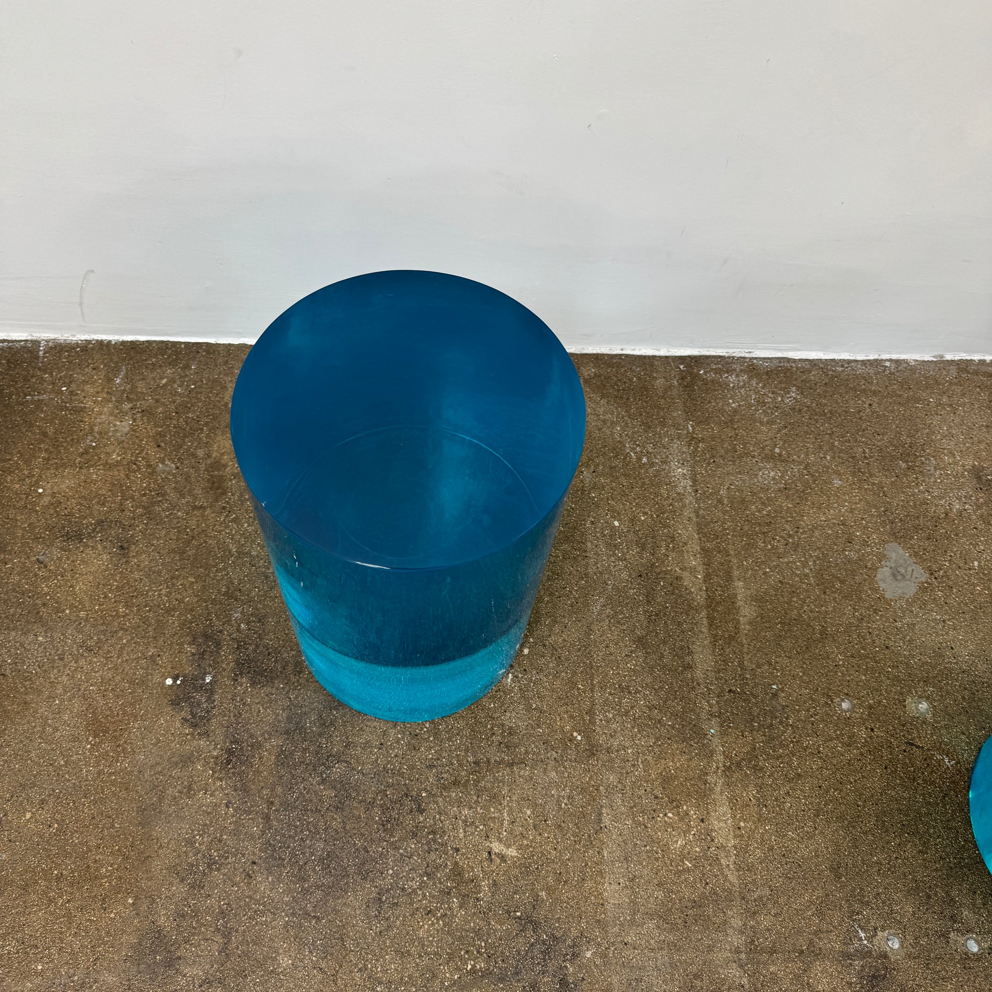 The Jonathan Adler blue acrylic cylindrical table stands upright on a white background, featuring smooth sides and a flat top that evoke the brand’s modern, chic design aesthetic.
