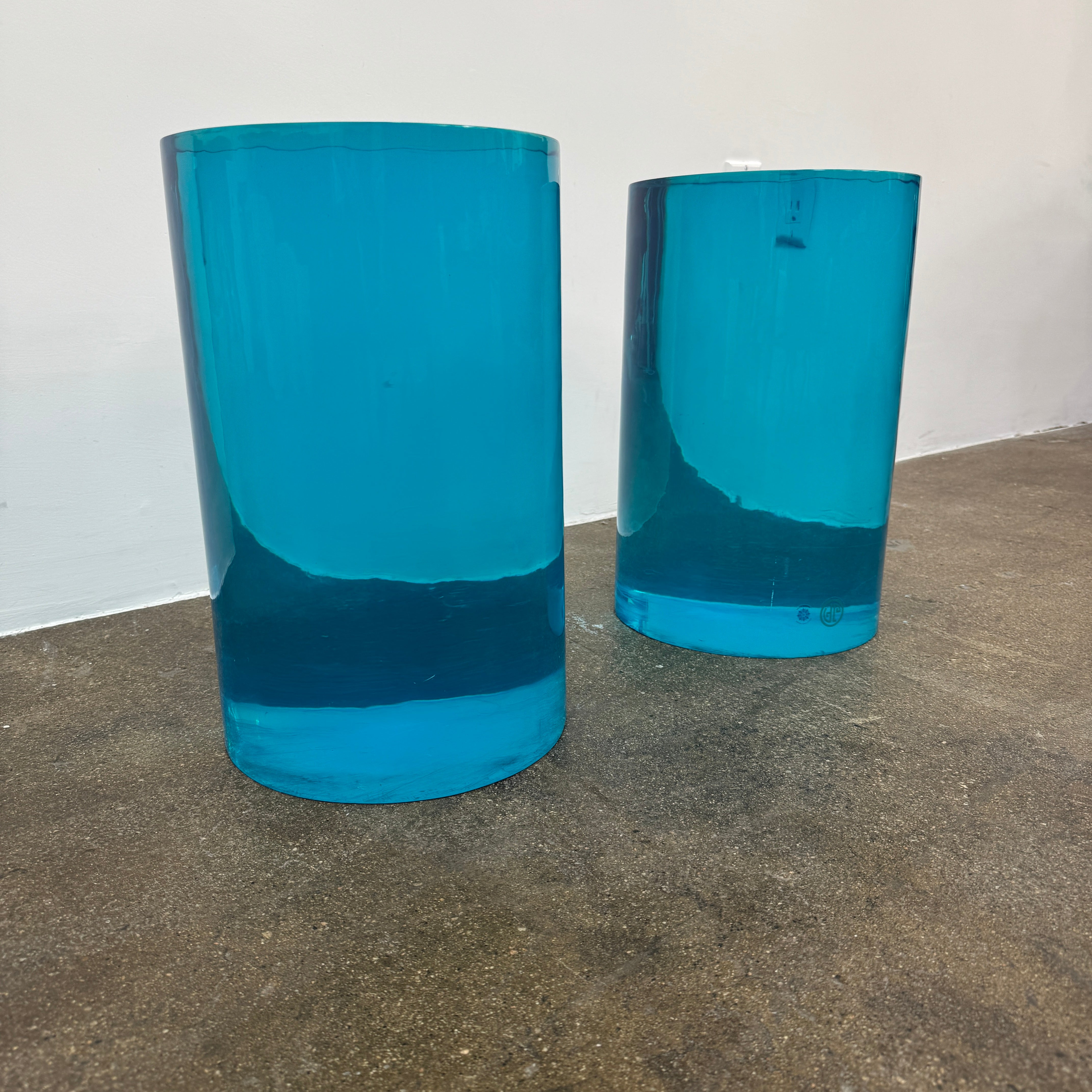 The Jonathan Adler blue acrylic cylindrical table stands upright on a white background, featuring smooth sides and a flat top that evoke the brand’s modern, chic design aesthetic.