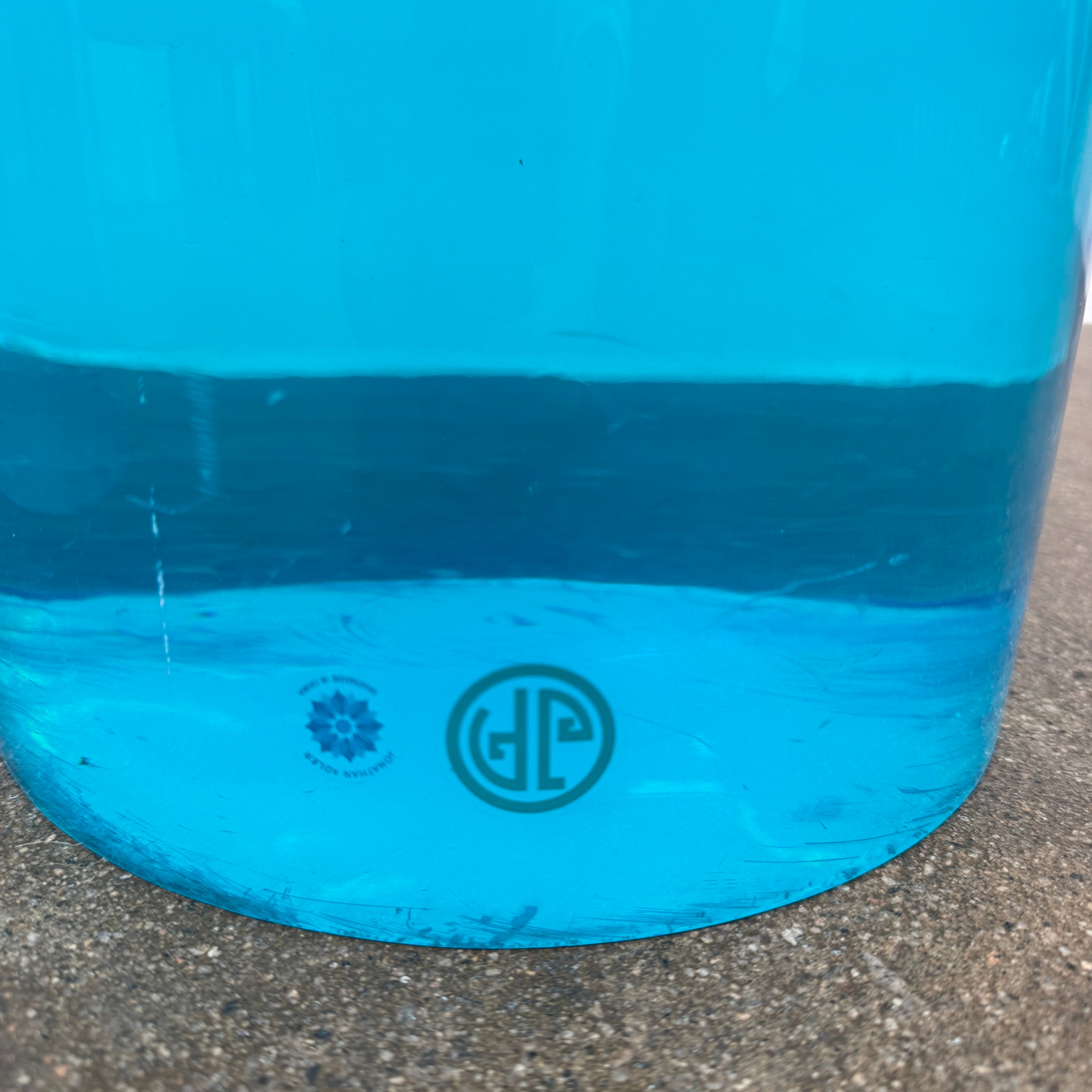 The Jonathan Adler blue acrylic cylindrical table stands upright on a white background, featuring smooth sides and a flat top that evoke the brand’s modern, chic design aesthetic.