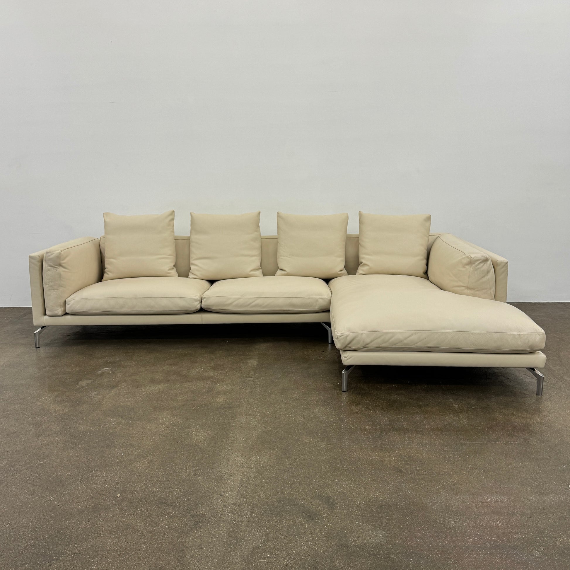 The DWR Como Sectional Sofa by DWR, in beige, features five back cushions and metal legs, showcasing Italian designer inspiration against a white background.
