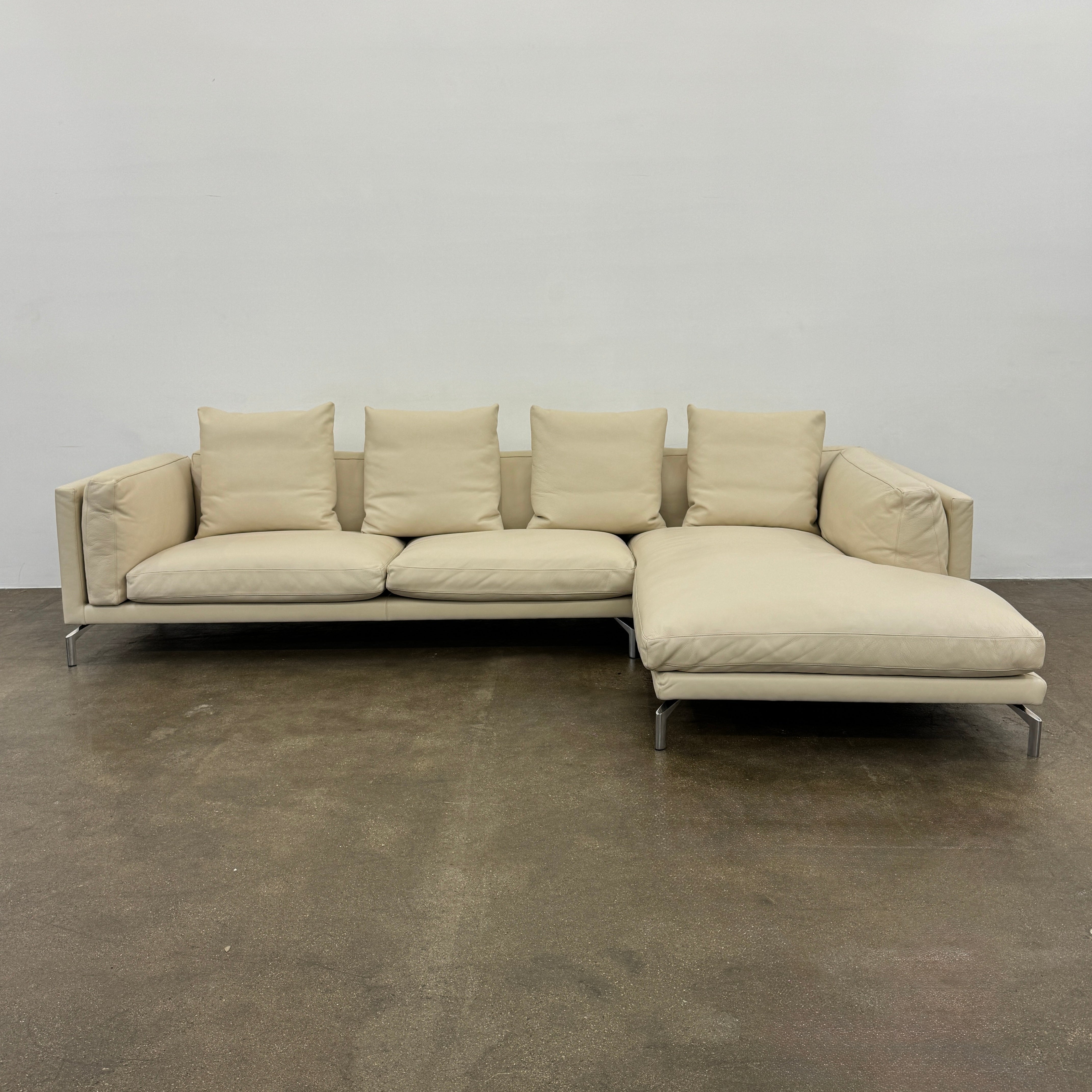 The DWR Como Sectional Sofa by DWR, in beige, features five back cushions and metal legs, showcasing Italian designer inspiration against a white background.